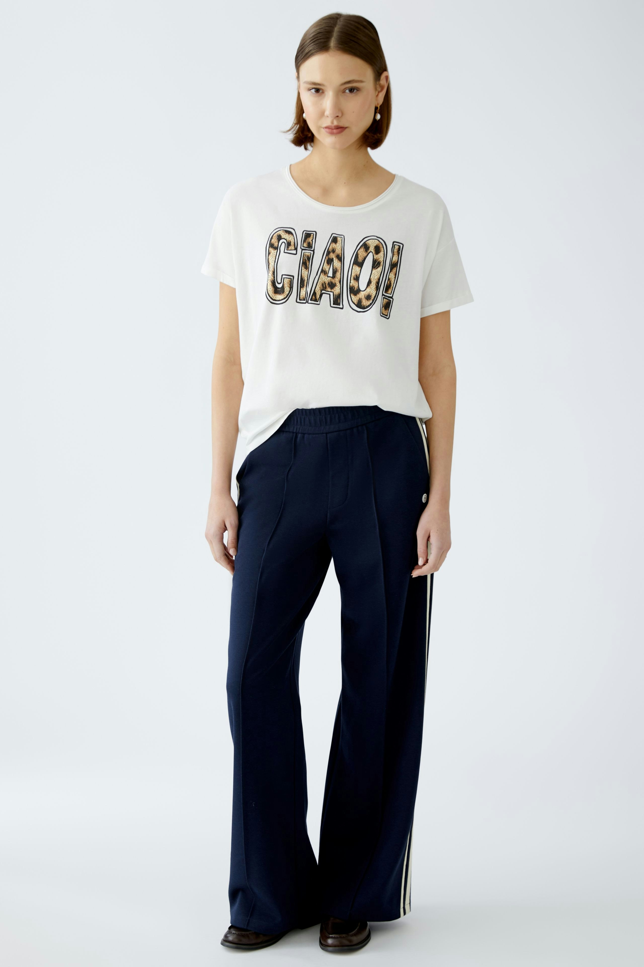 Stylish women's T-shirt: A woman in a white tee with 'CIAO' print, paired with navy trousers.