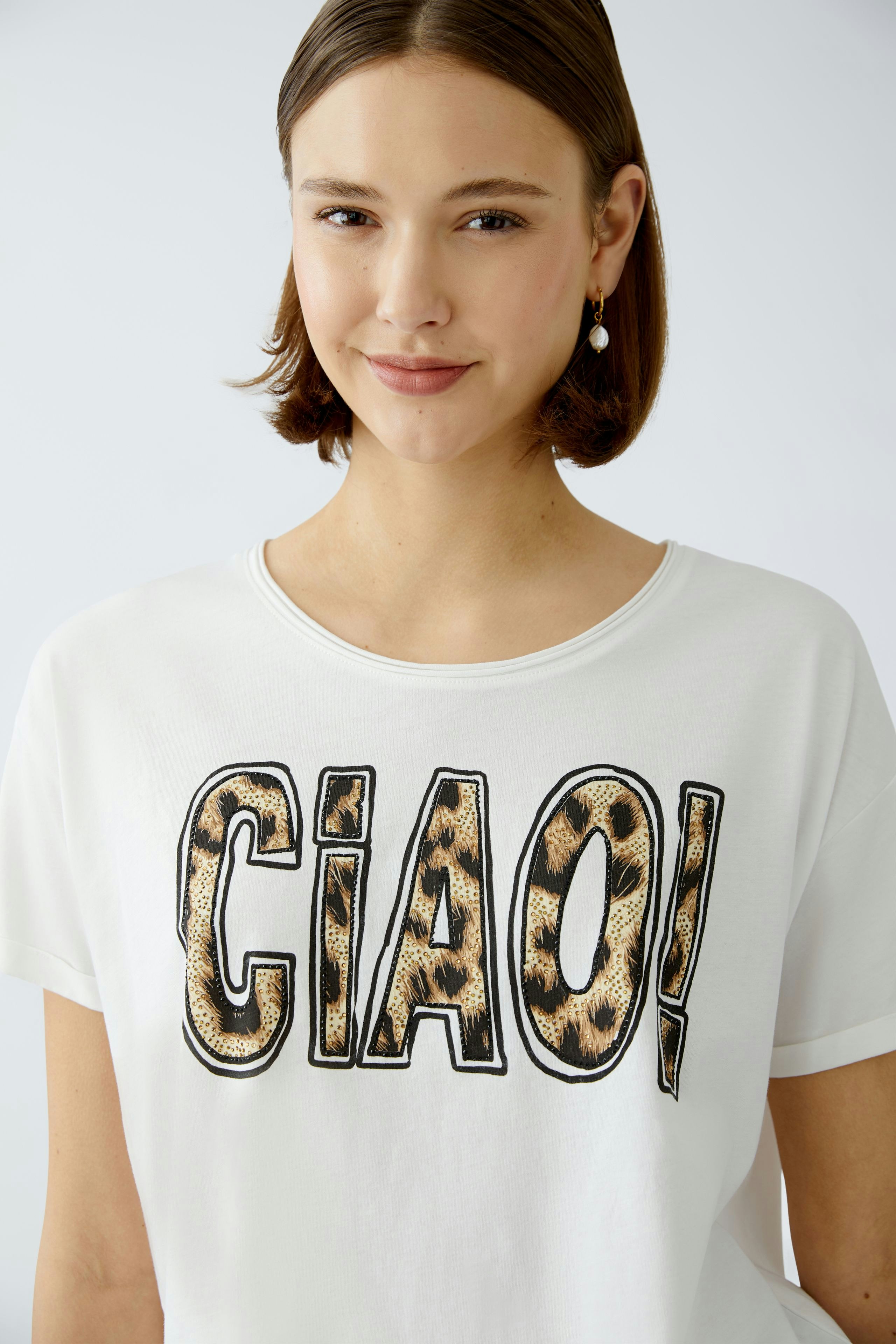 Stylish women's T-shirt: A woman in a white tee with a bold 'CIAO!' print, exuding casual elegance.