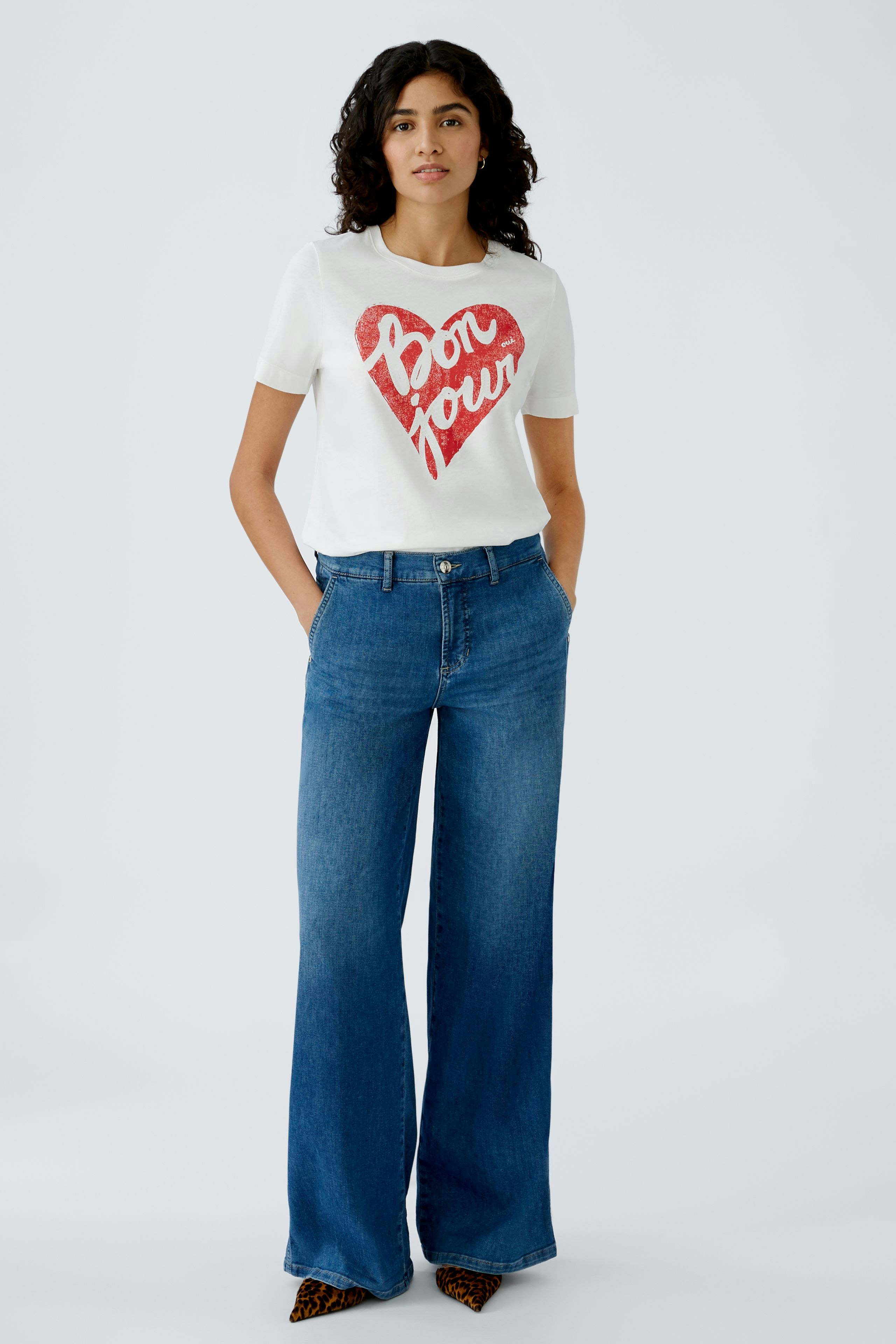 Stylish women's T-shirt: A woman in a white tee with a red heart design and relaxed fit jeans.