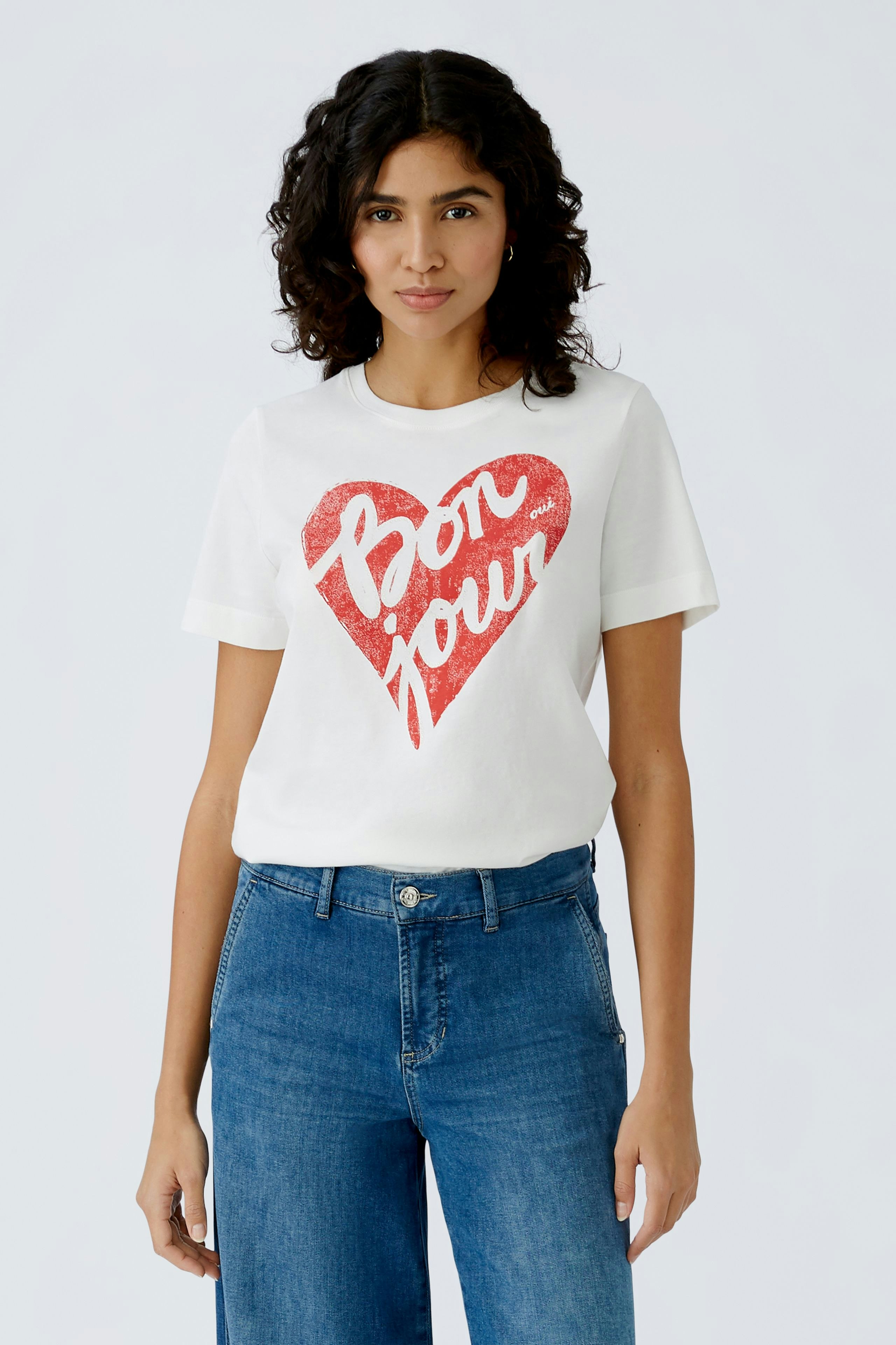 Stylish women's T-shirt: A woman in a white tee with a red heart and 'Bonjour' print, paired with blue jeans.