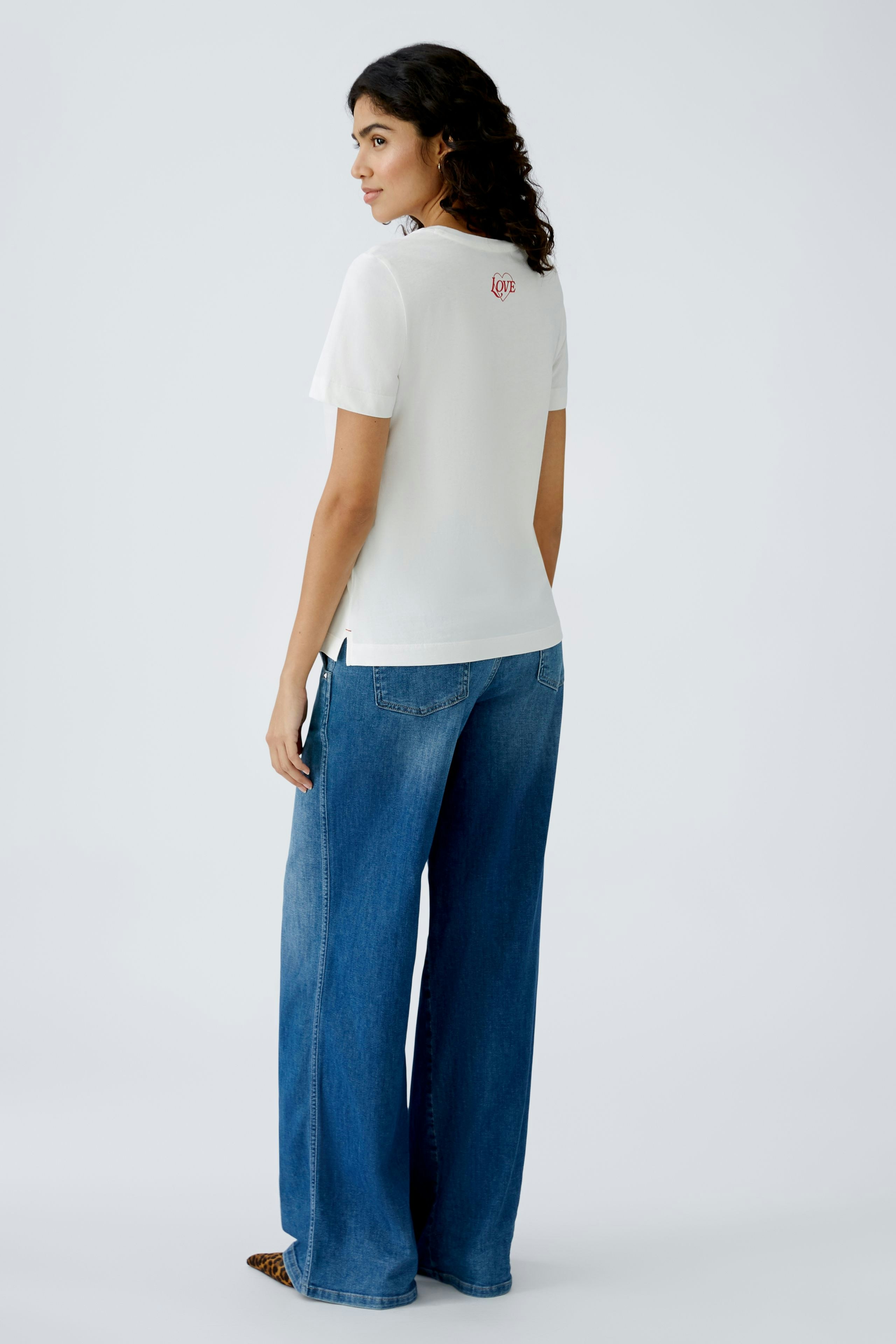 Stylish women's T-shirt: A woman in a white tee with a subtle logo, paired with wide-leg jeans.