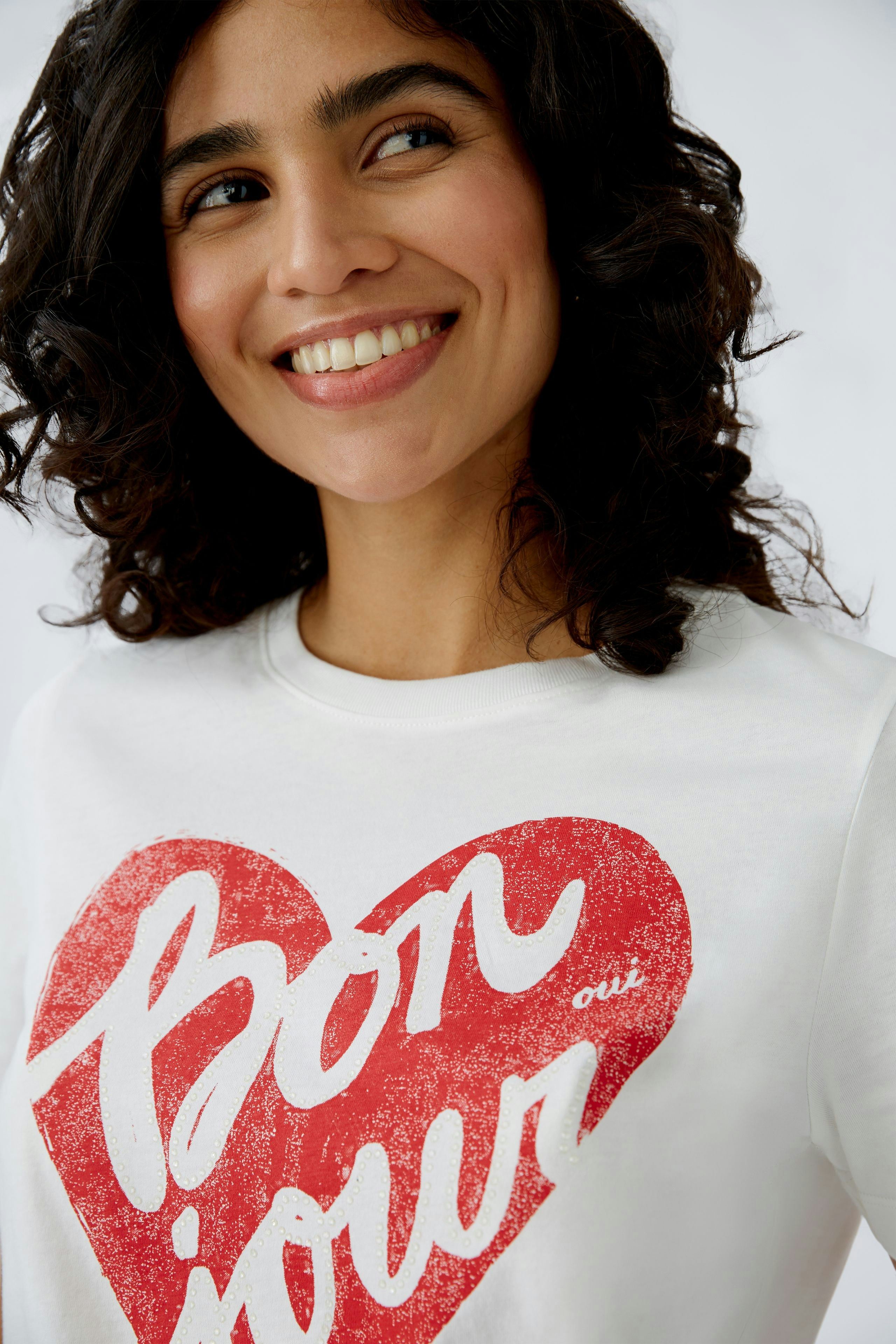 Stylish women's T-shirt: A woman smiles in a white tee with a red heart and 'Bonjour' print.