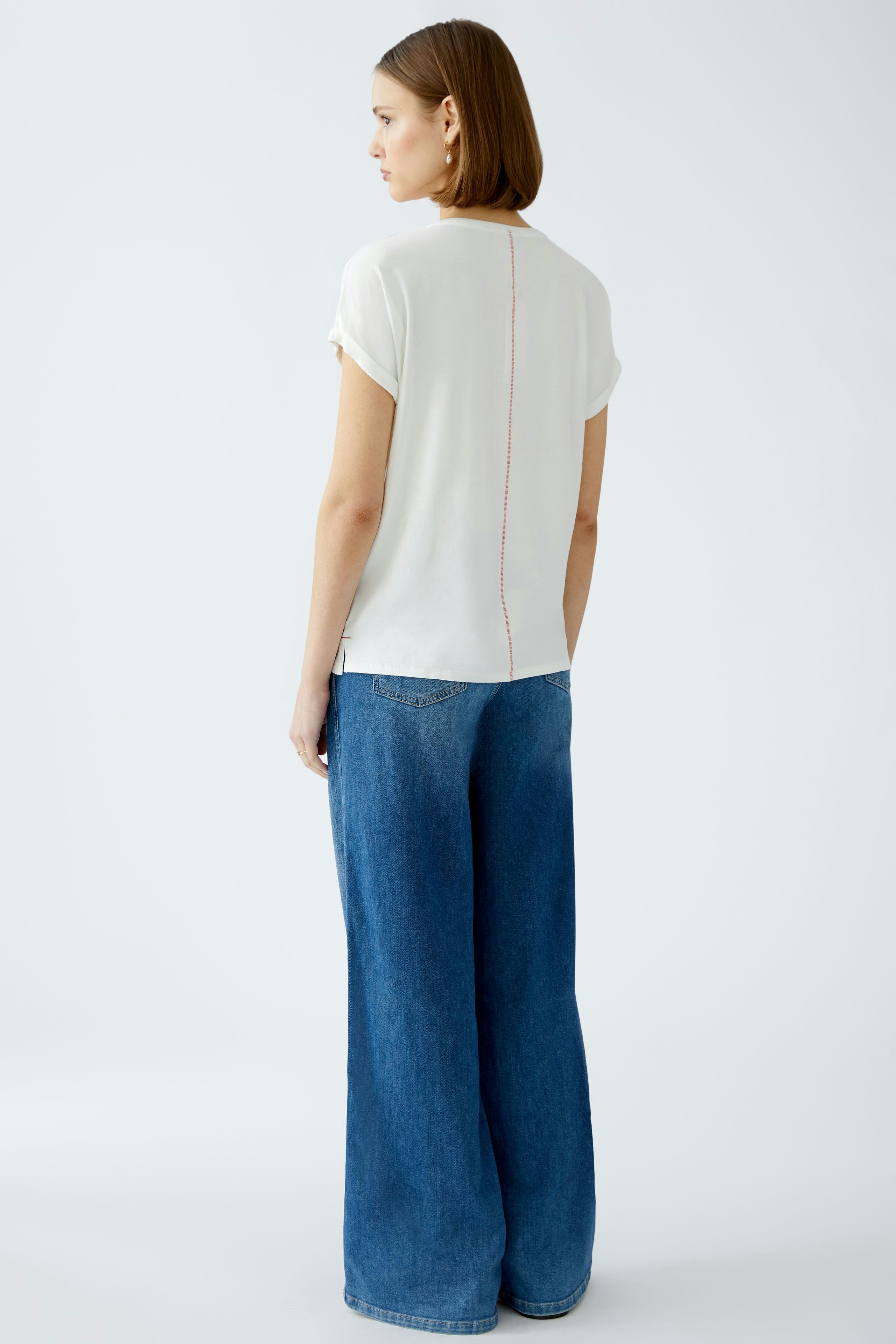Elegantes Damen-T-Shirt: Frau trägt ein schlichtes, weißes T-Shirt mit dezentem Design und lässigen Jeans.