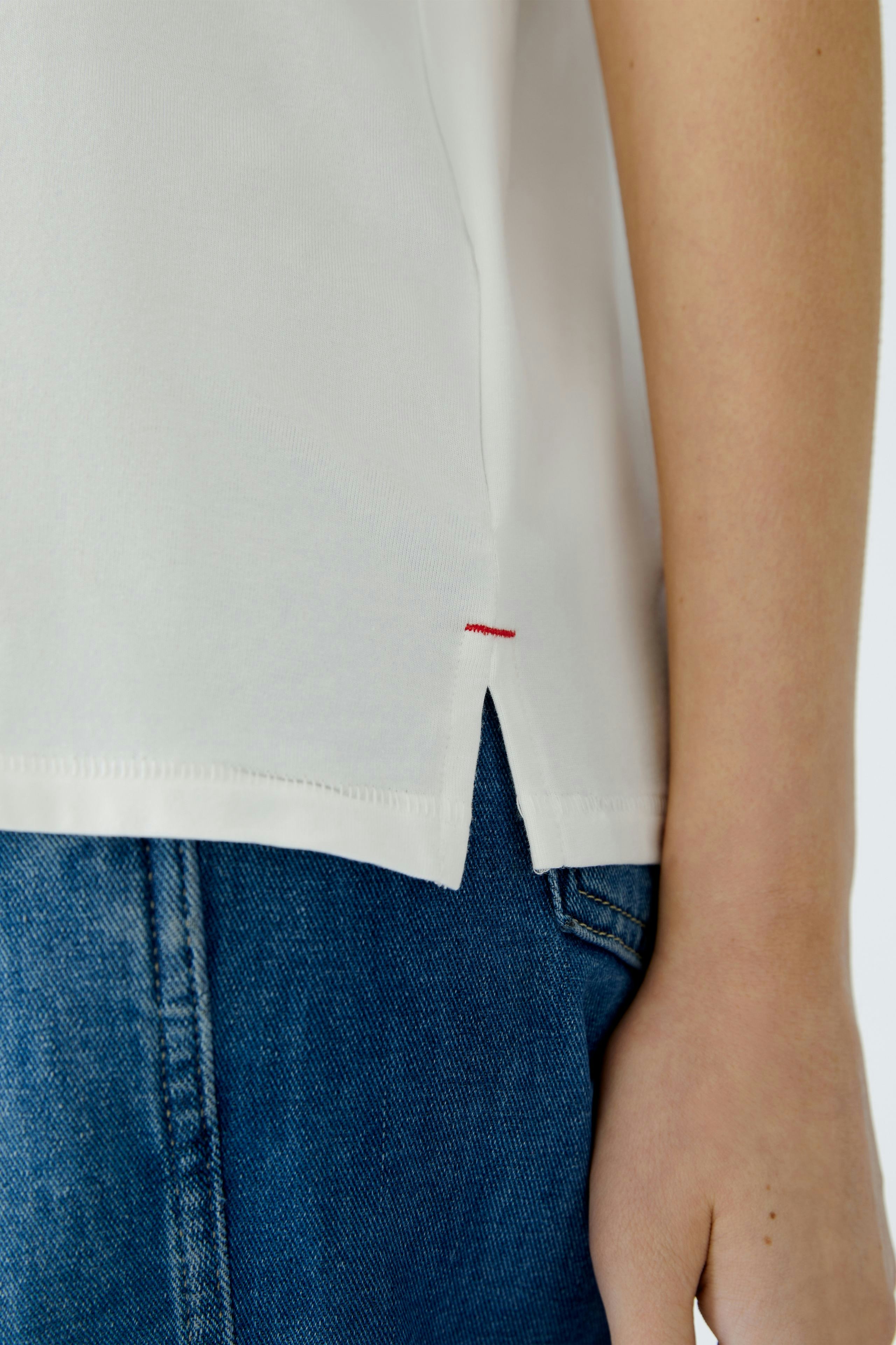 Elegantes Damen-T-Shirt: Frau trägt ein weißes T-Shirt mit seitlichem Schlitz und lässiger Jeans.