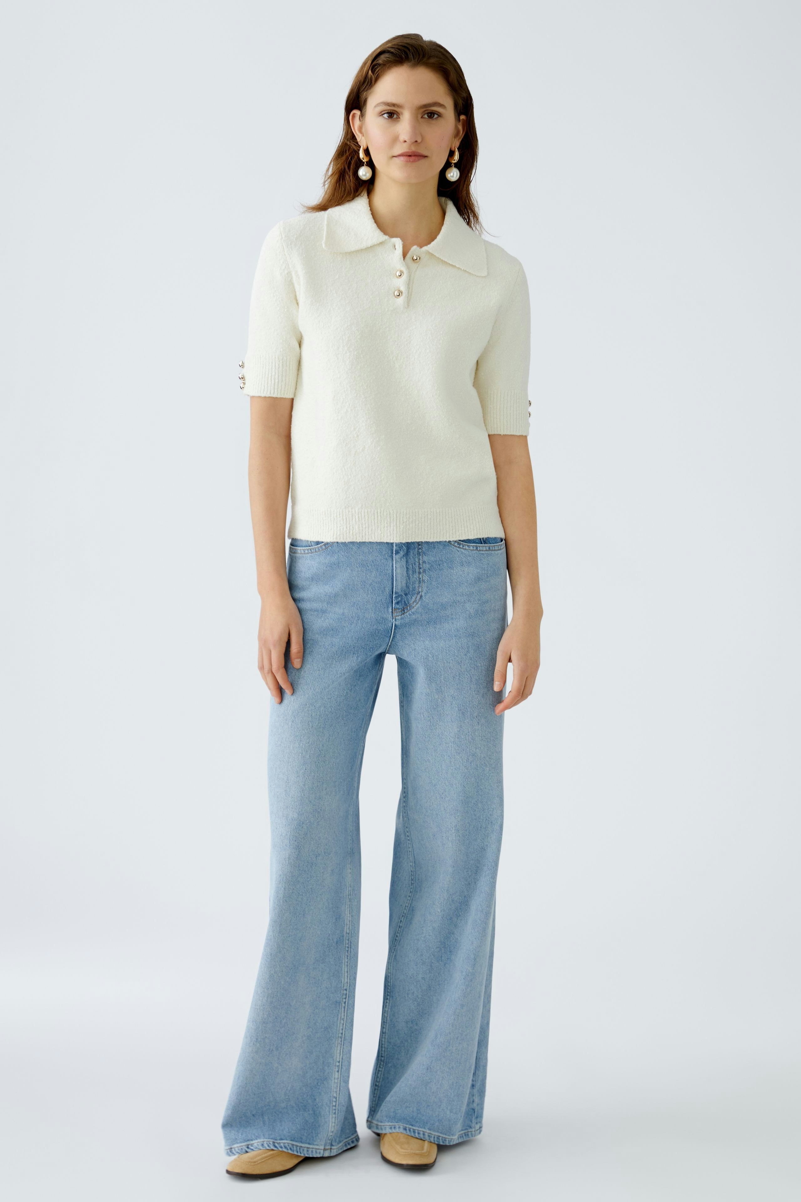 Stylish women's pullover: A woman in a cream short-sleeve pullover with buttons, paired with flared jeans.