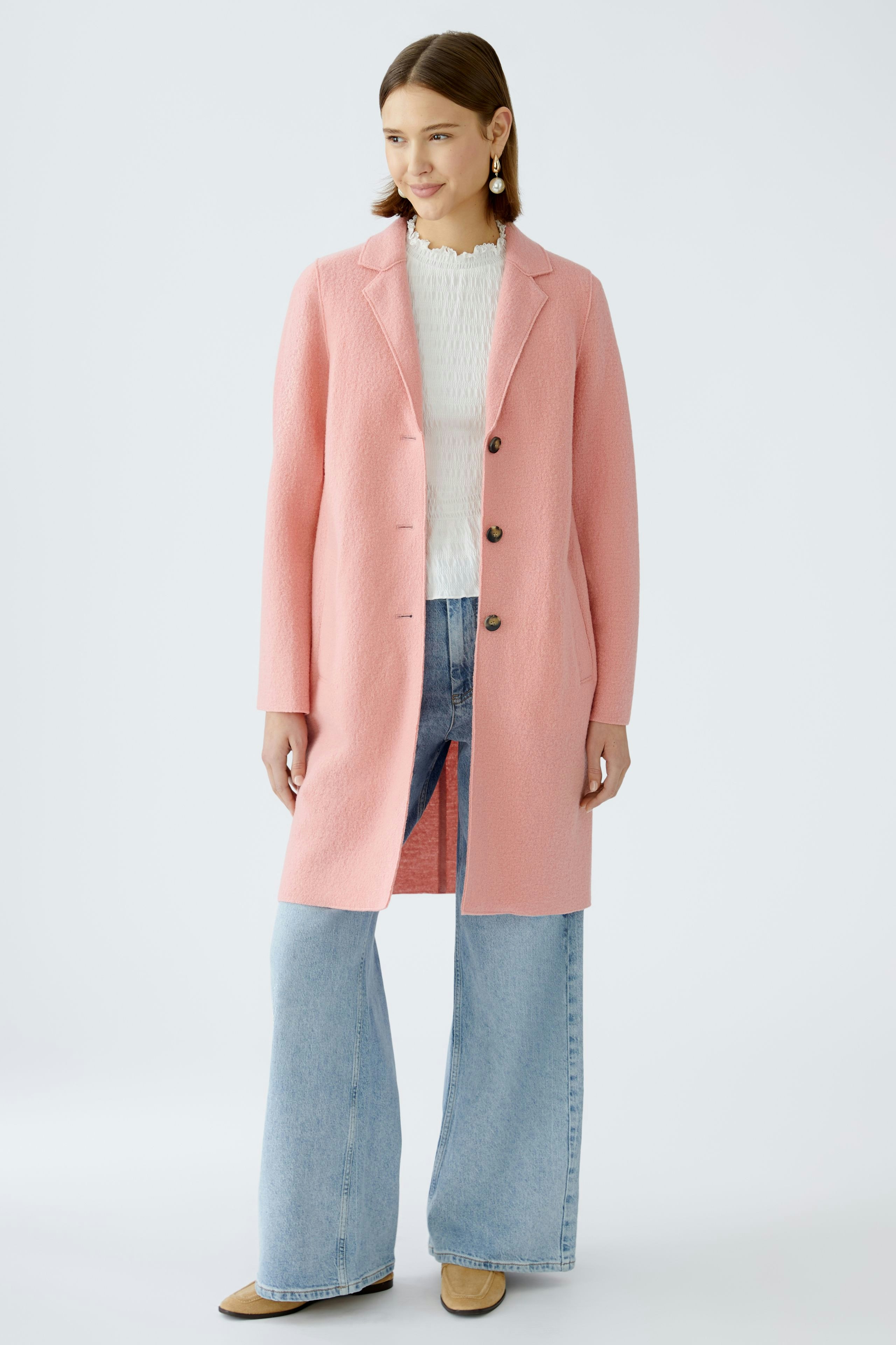 Stylish women's coat: A woman in a pink coat over a white top and jeans, exuding elegance.