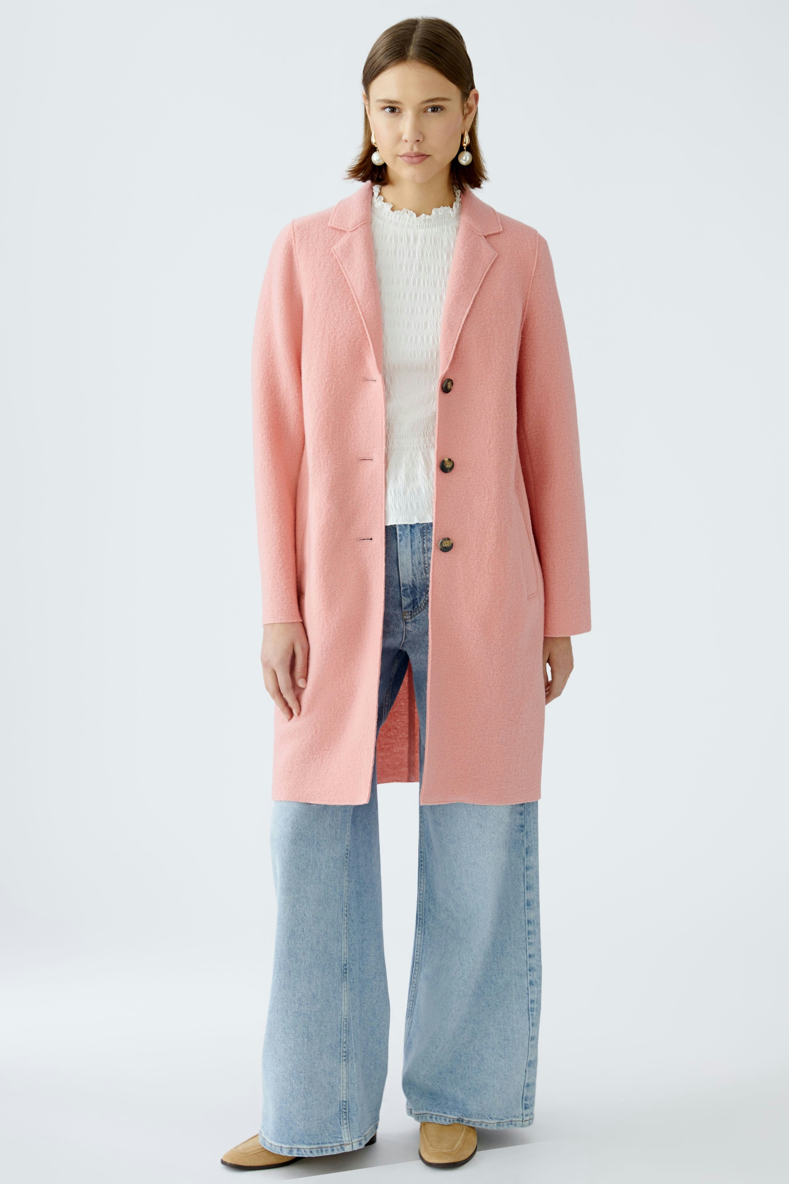 Stylish women's coat: A woman in a pink coat over a white top and wide jeans stands confidently.
