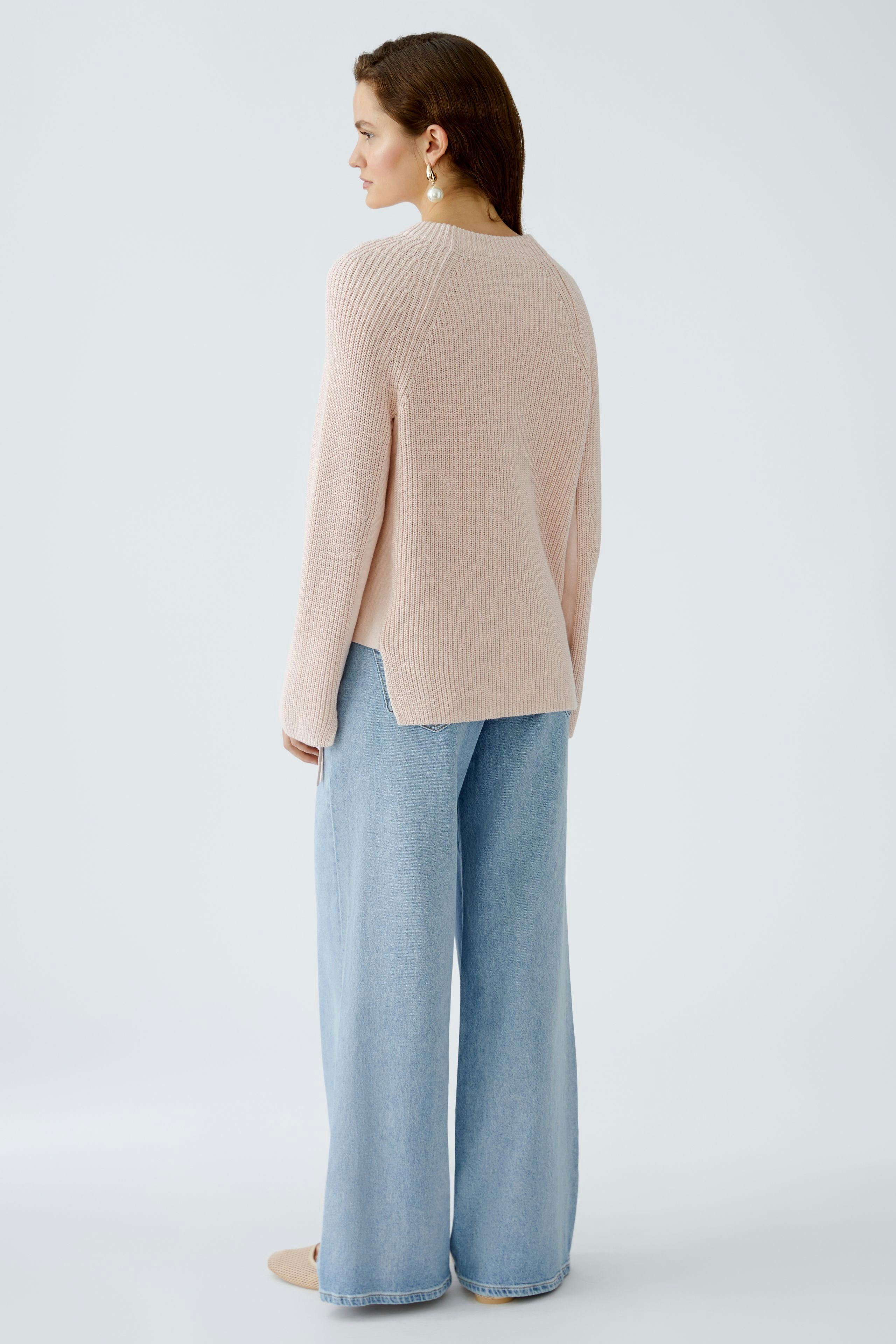 Damen-Pullover: Frau in zartem rosa Strickpullover mit lässigem Schnitt und weiten Jeans.