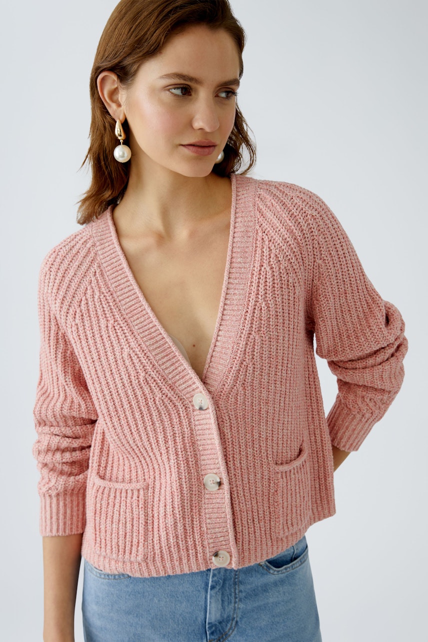 Feminine Strickjacke: Junge Frau in einer rosa Strickjacke mit Knöpfen und Taschen, lässig und stilvoll.