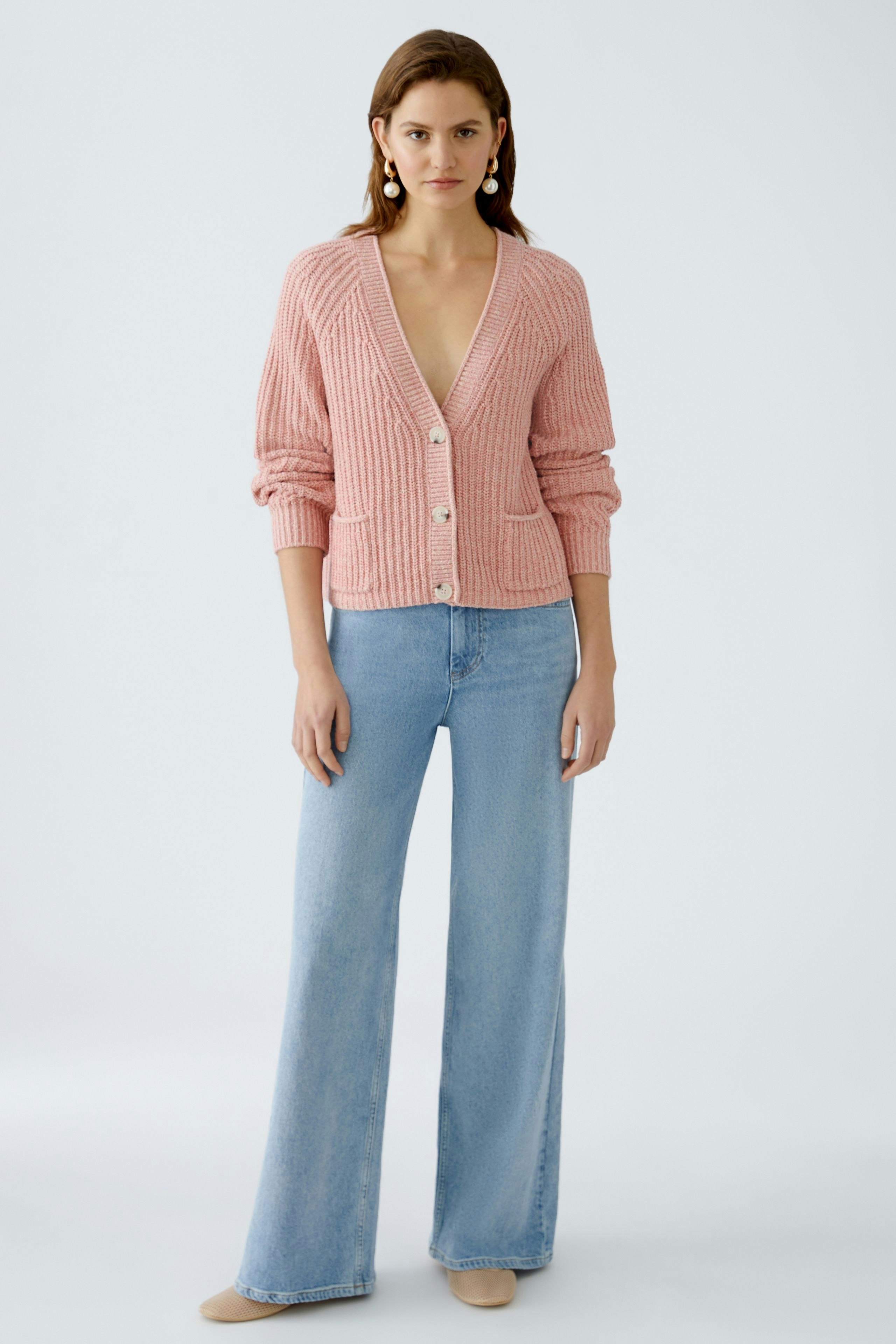 Stylish women's cardigan: A woman in a pink knitted cardigan with buttons and pockets, paired with jeans.