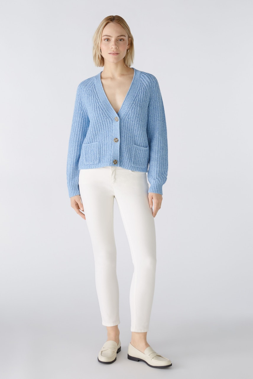 Stylish women's cardigan: A woman in a light blue cardigan with pockets and buttons, paired with white pants.