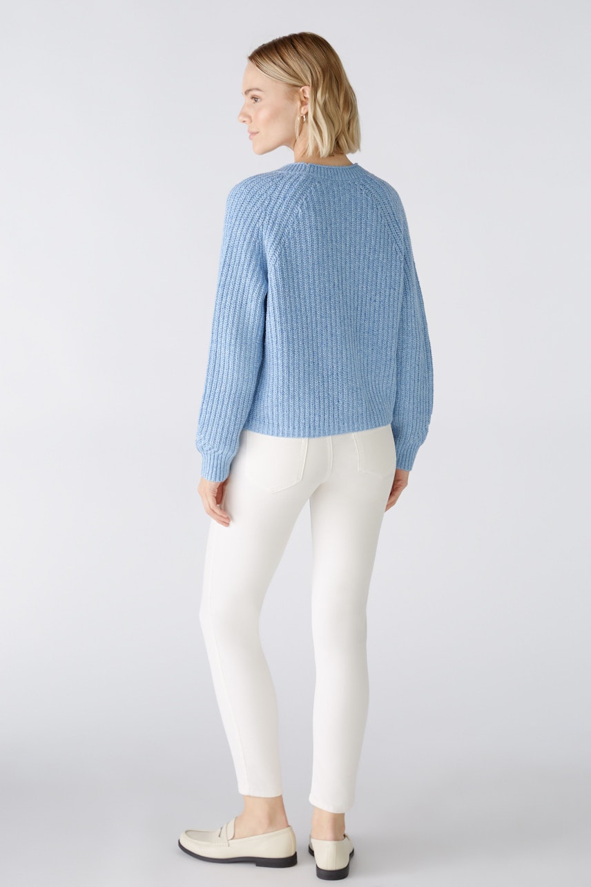 Stylish women's cardigan: A woman in a light blue knitted cardigan paired with white pants.