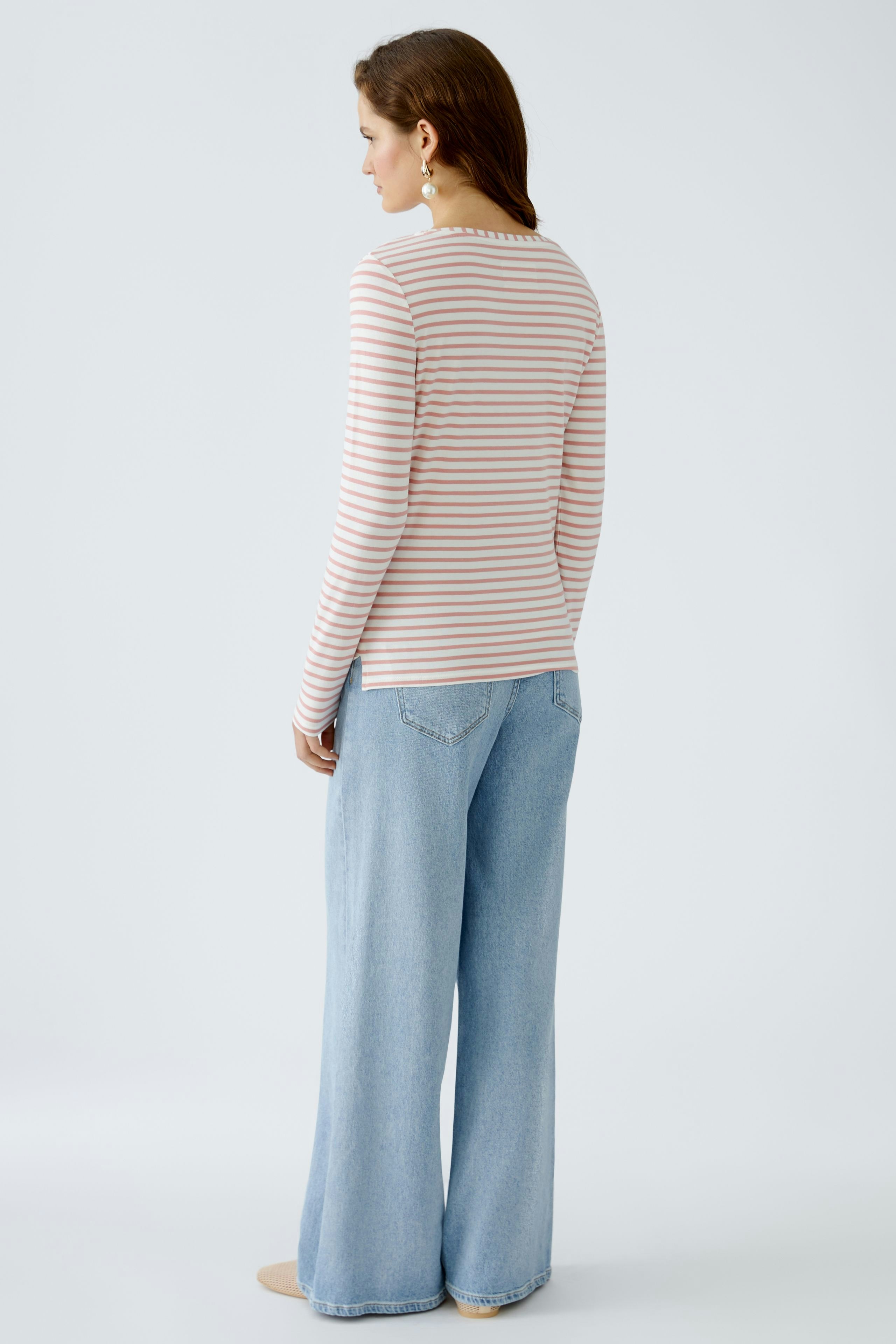 Langarmshirt: Frau trägt ein gestreiftes Langarmshirt in sanften Farben, kombiniert mit lässigen Jeans.