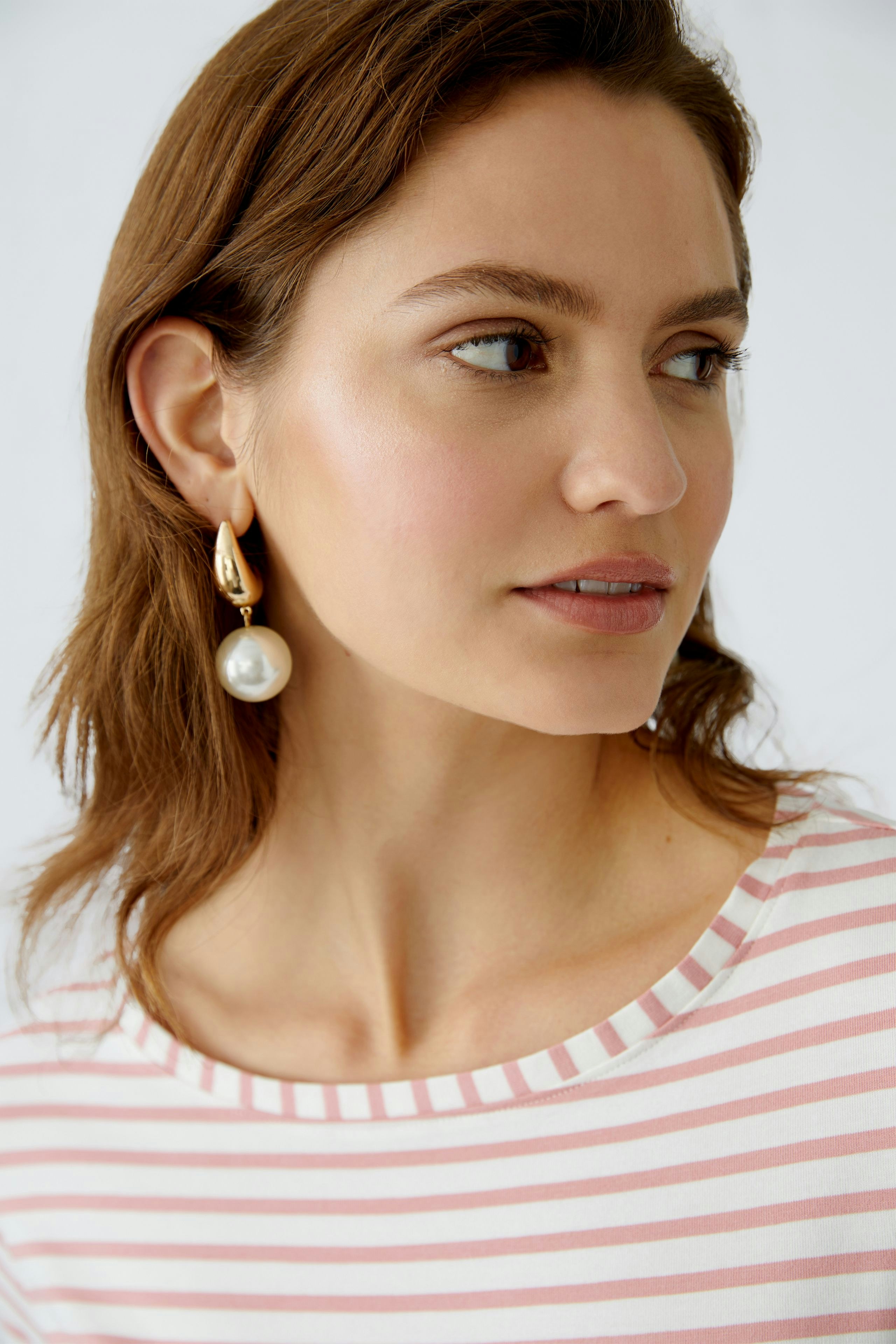 Damen Langarmshirt: Junge Frau mit gestreiftem Shirt und eleganten Ohrringen blickt nachdenklich.