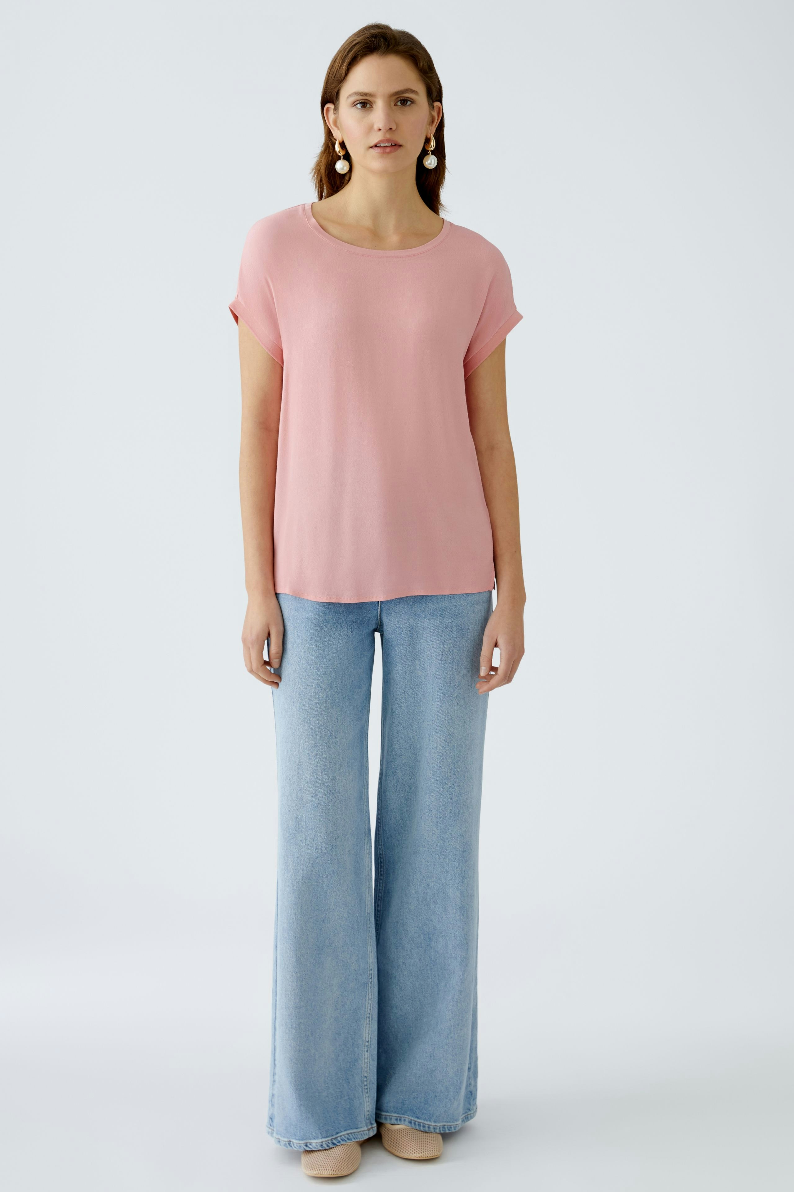 Leichtes Blusenshirt in zartem Rosa: Frau trägt es mit lässigen Jeans und strahlt Eleganz aus.