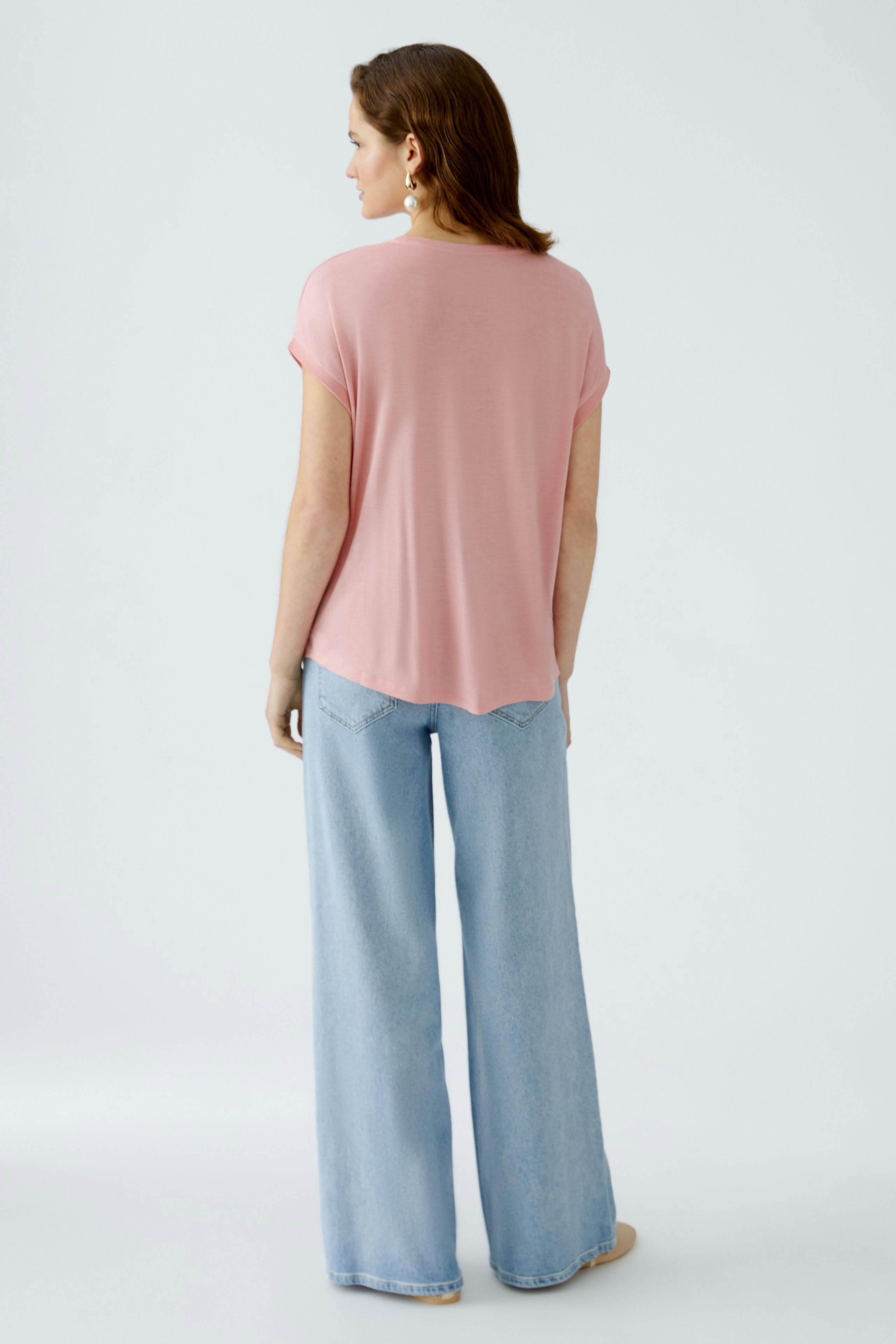 Bequemes Blusenshirt: Frau in einem rosafarbenen Shirt mit lässigem Schnitt und weiten Jeans von hinten.