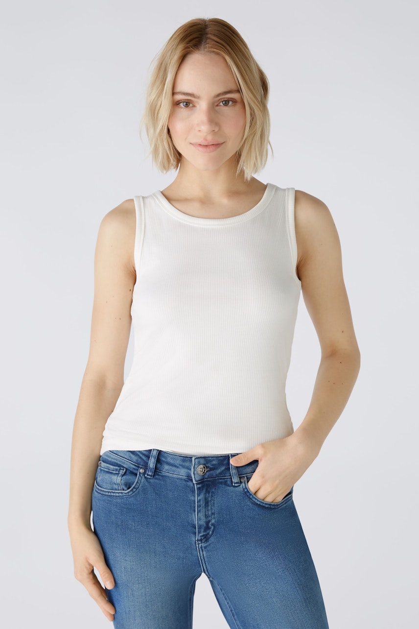 Stylish women's top: A woman in a white sleeveless top paired with blue jeans, exuding casual elegance.