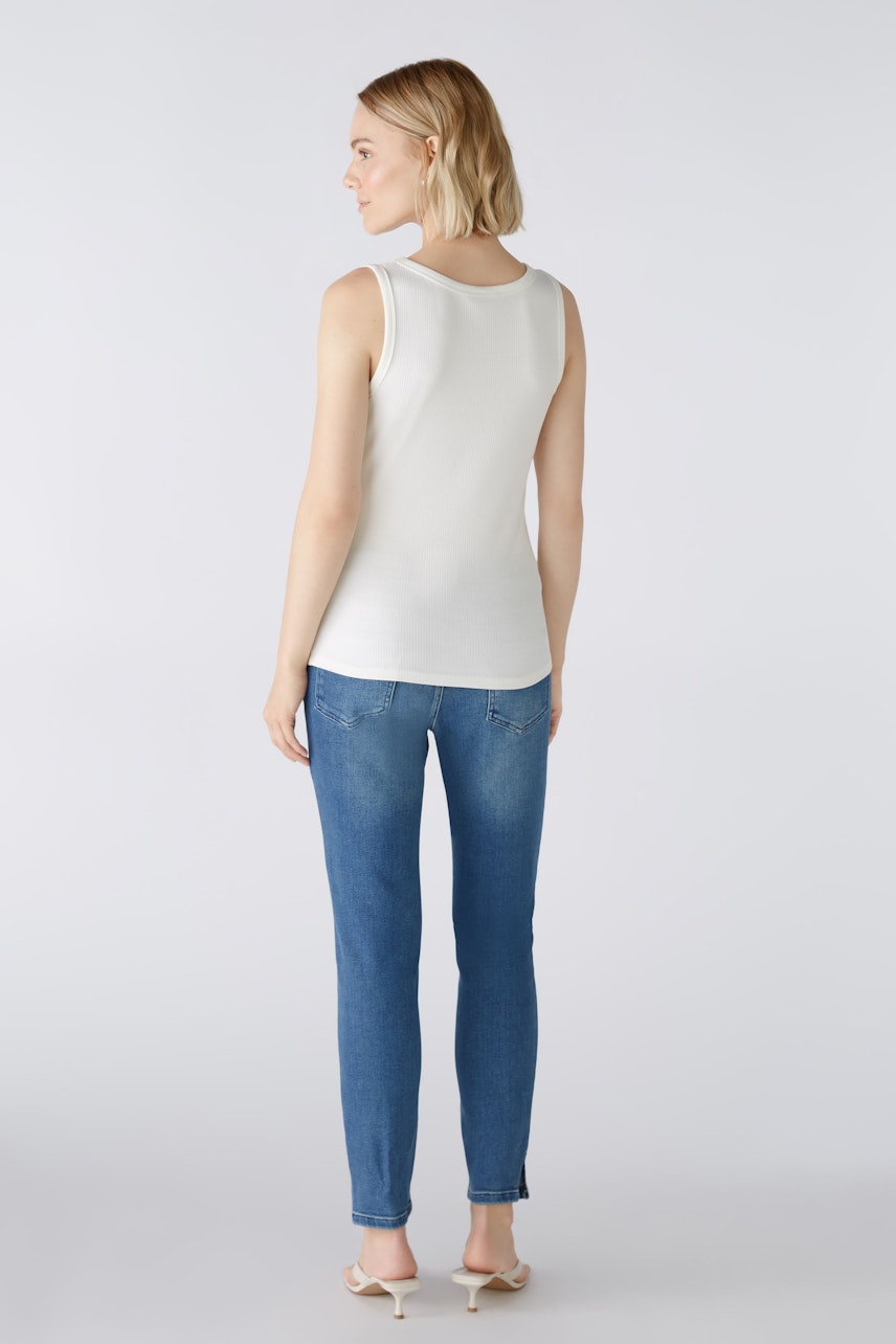 Stylish women's top: A woman in a white sleeveless top paired with blue jeans, showcasing a casual look.