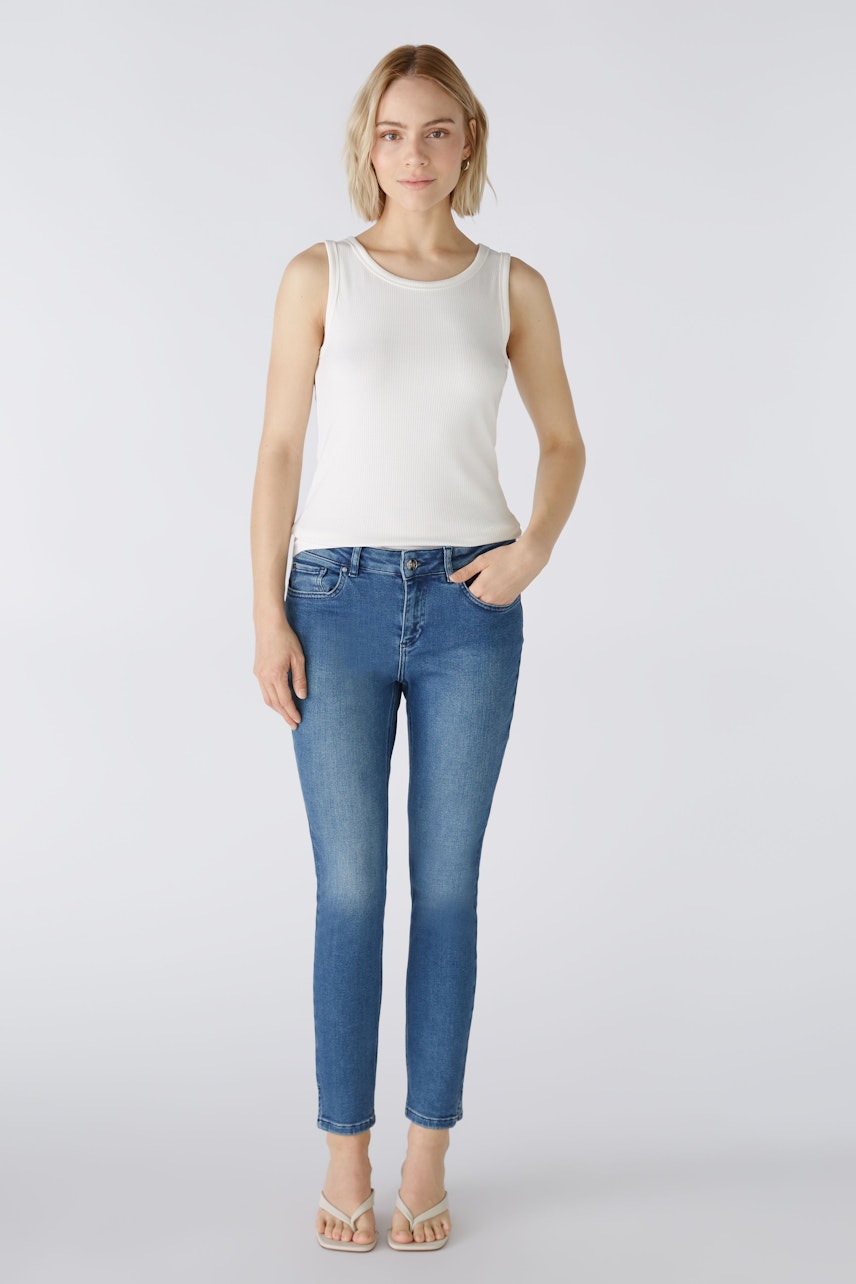 Stylish women's top: A woman in a white sleeveless top paired with blue jeans, exuding casual elegance.