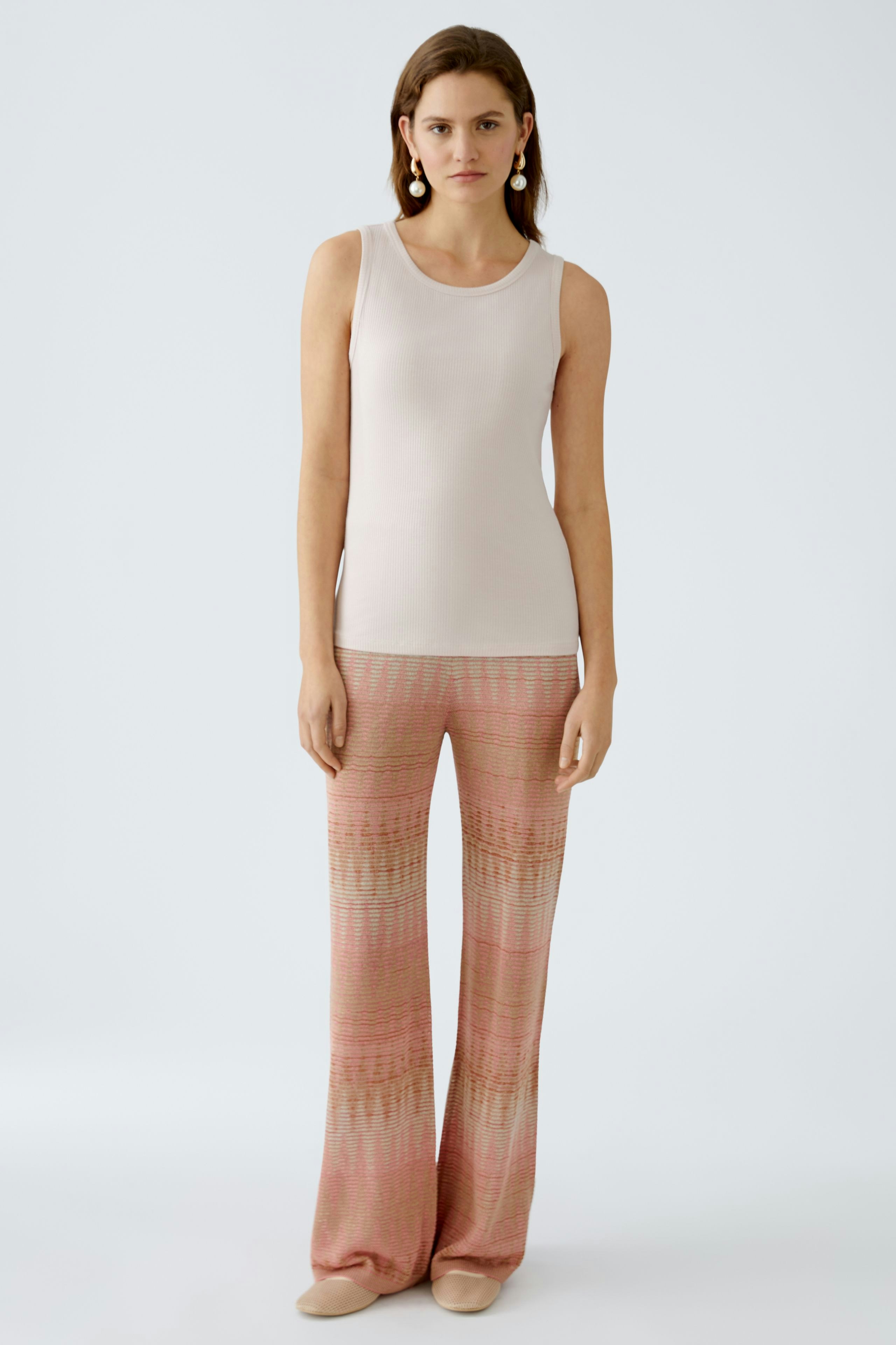 Elegant women's top: A woman in a light tank top paired with patterned flared pants.