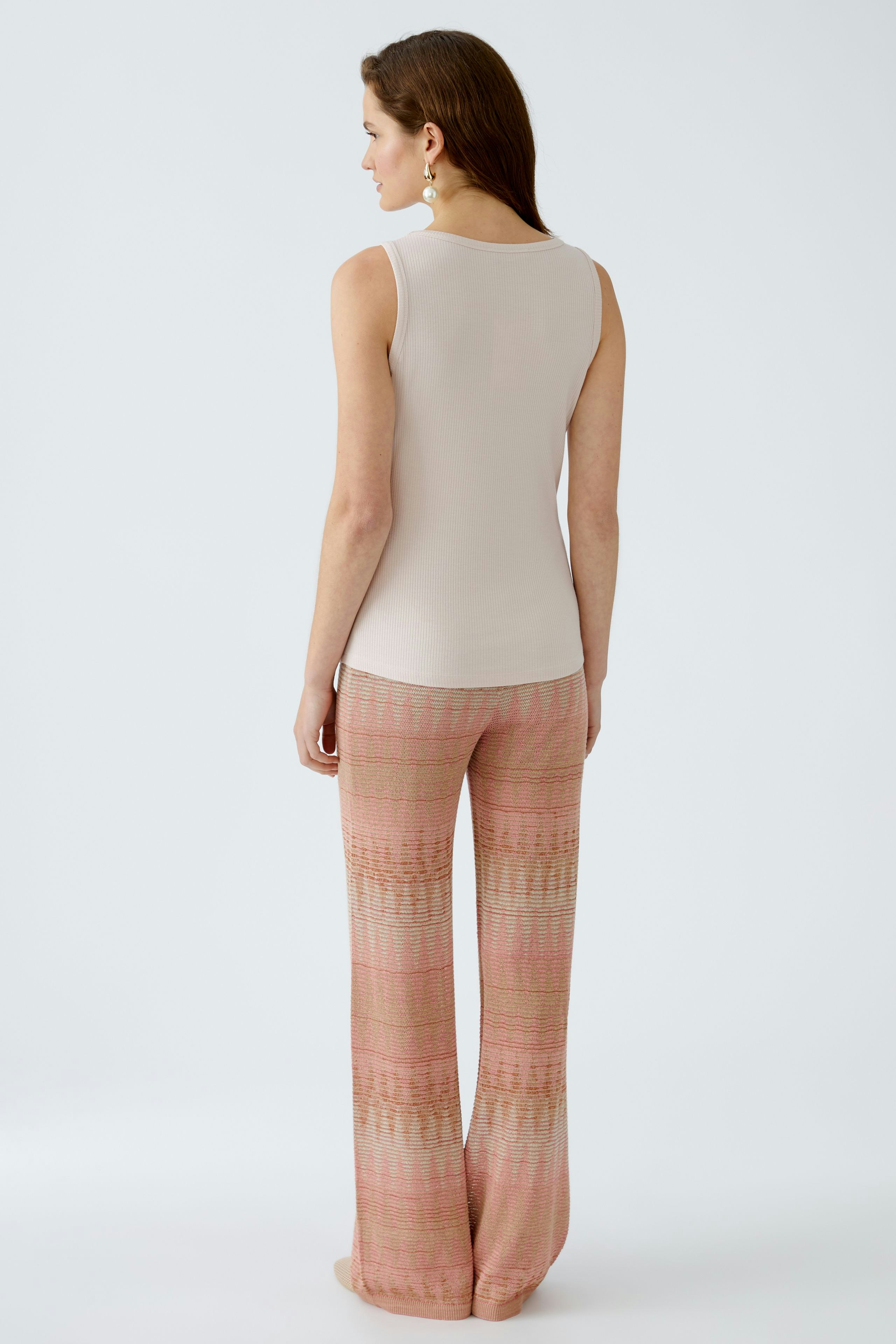 Elegant women's top: A woman in a fitted beige sleeveless top paired with patterned flared pants.