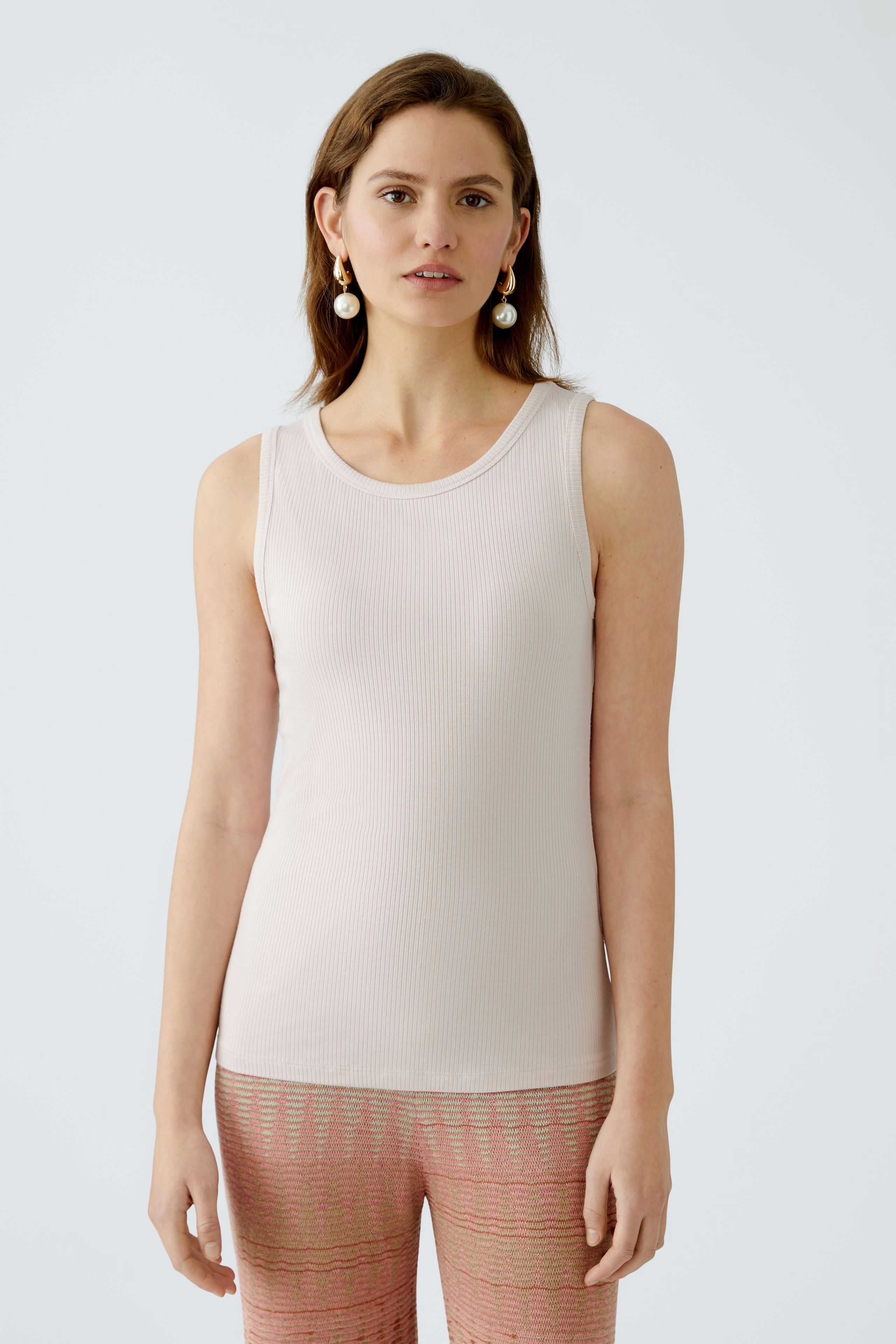 Elegant women's top: A woman in a light pink sleeveless top, paired with patterned pants.