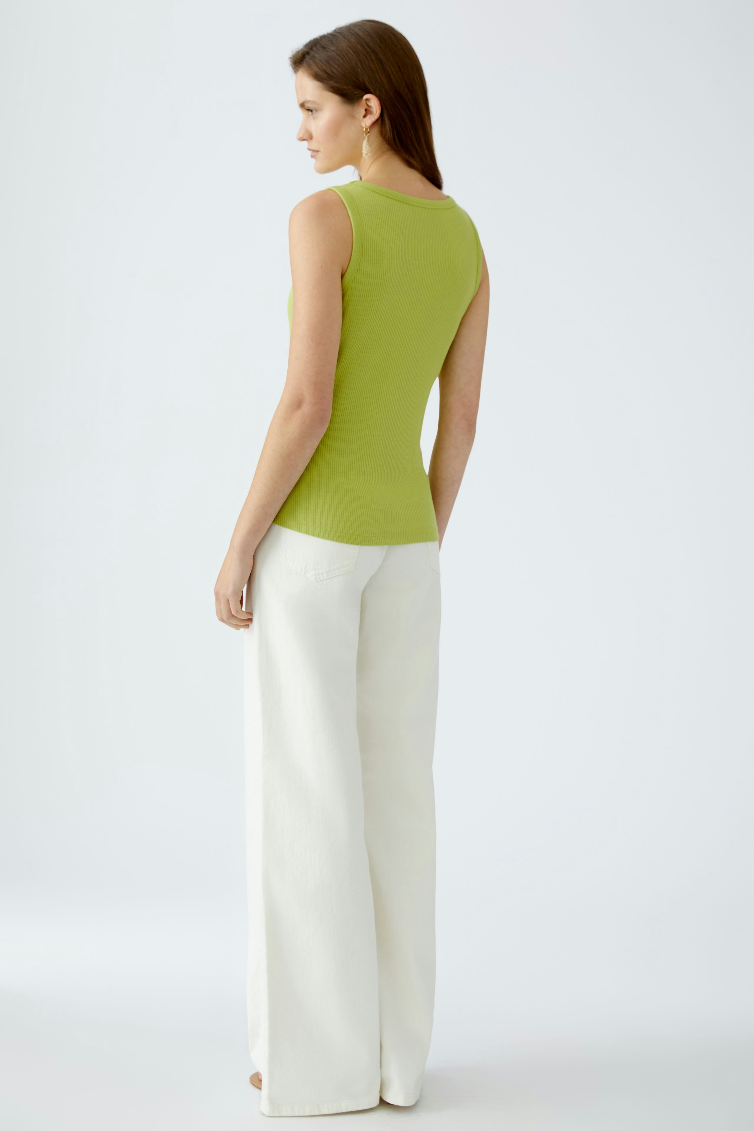 Elegantes Damen-Top: Frau in grünem, ärmellosem Oberteil mit lässigen, weißen Hosen.