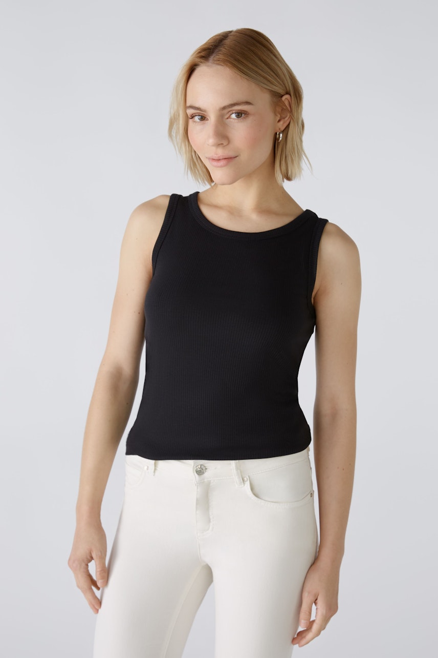 Stylish women's top: A woman in a black sleeveless top paired with white jeans, exuding confidence.