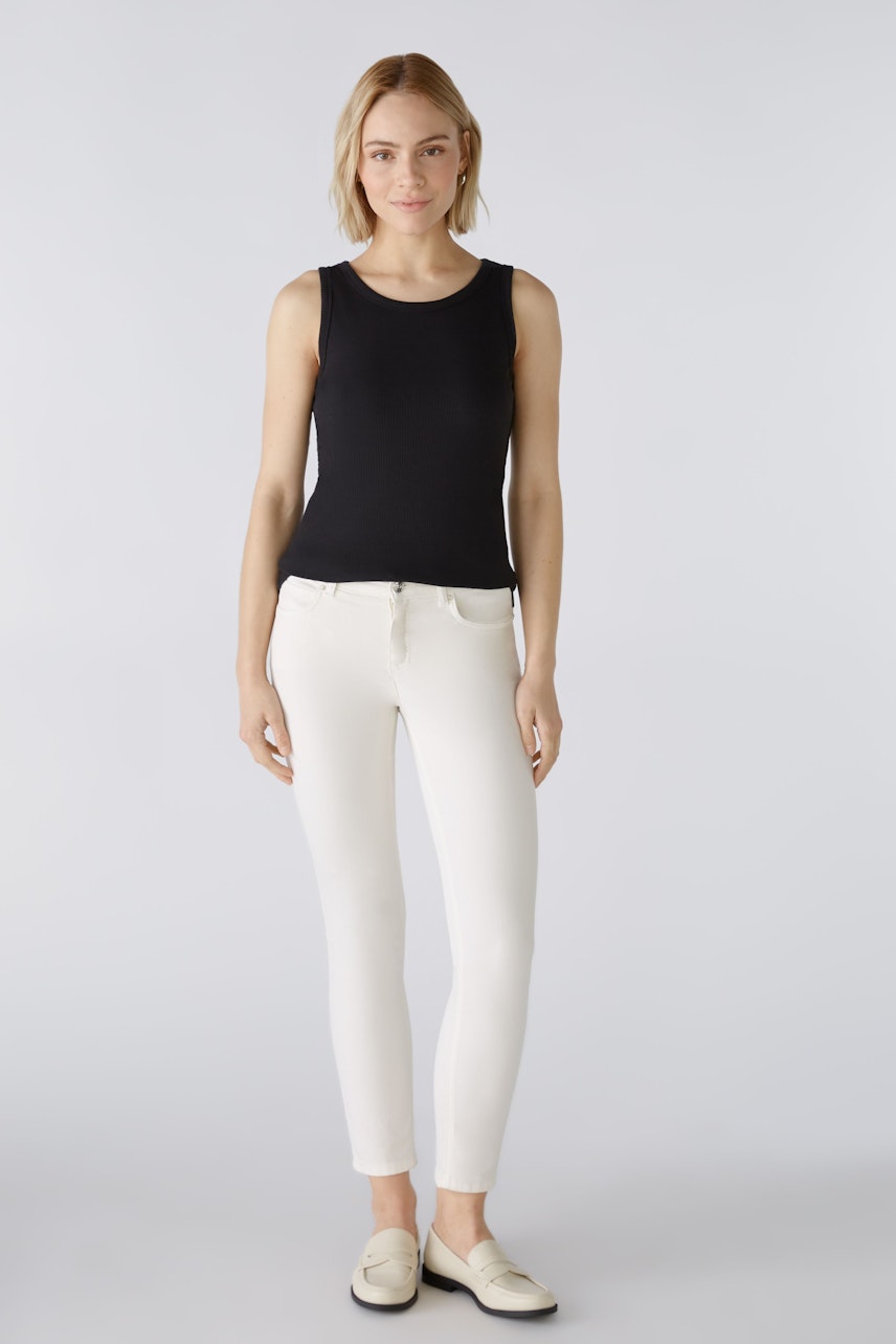 Stylish women's top: A woman in a black sleeveless top paired with white pants, exuding confidence.