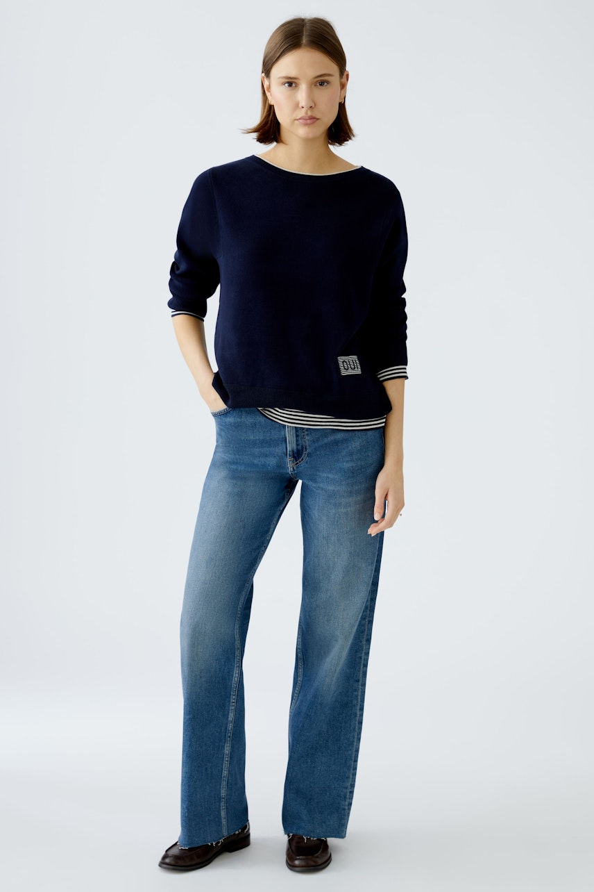 Modern women's pullover: A woman in a navy pullover with a casual striped shirt underneath.