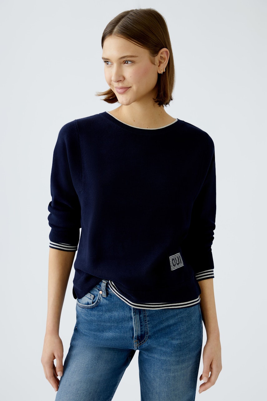 Modern women's pullover: A woman in a navy pullover with striped cuffs smiles confidently.