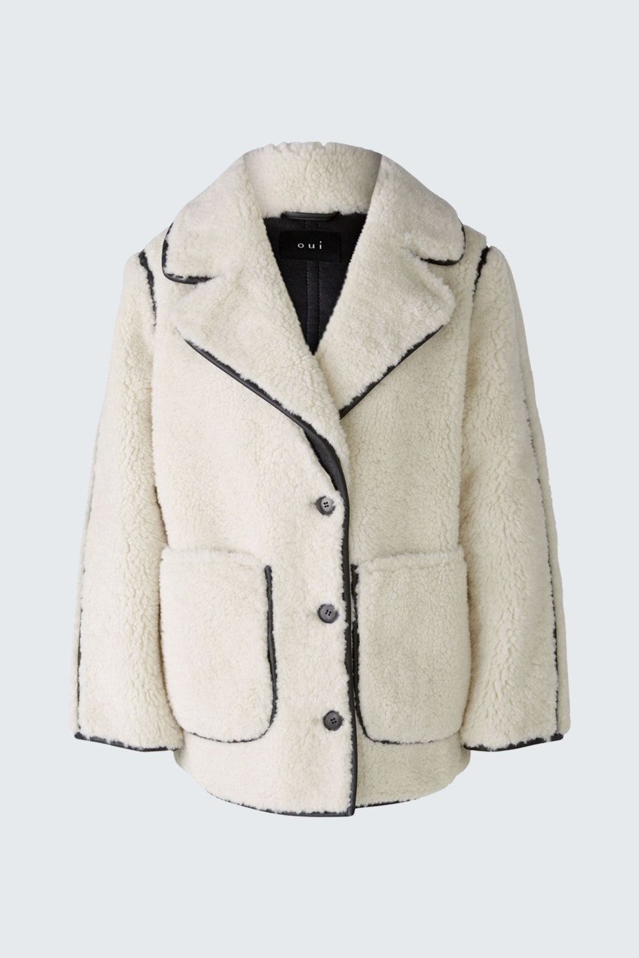 Chic women's coat: Stylish woman in a cream faux fur coat with black trim and pockets.