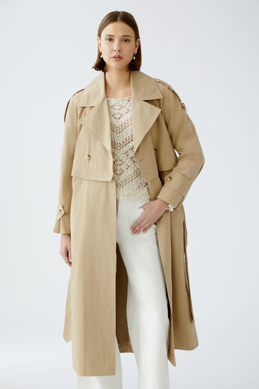 Stylish trench coat: A woman in a beige trench coat over a white top and light pants, exuding elegance.