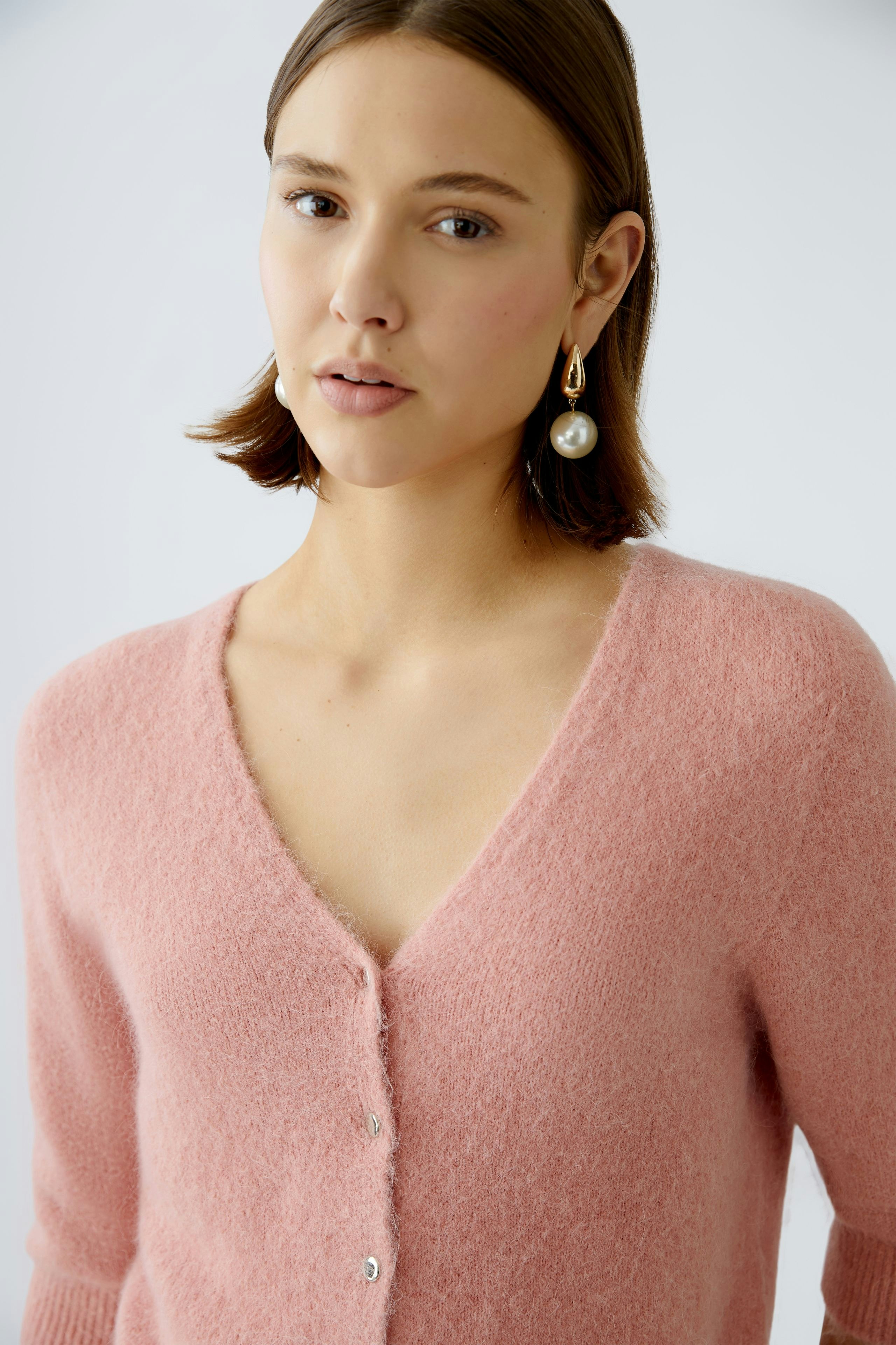 Feminine Strickjacke: Junge Frau in zarter rosa Strickjacke mit V-Ausschnitt und Knöpfen.