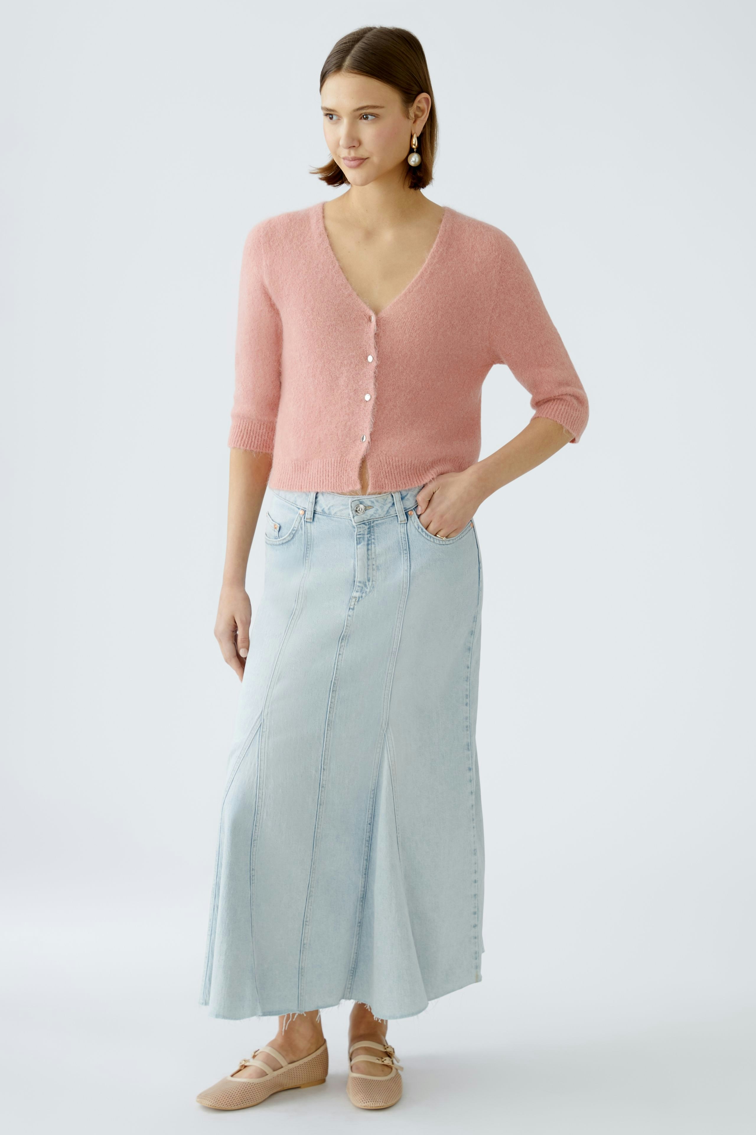 Feminine Strickjacke: Junge Frau in zarter rosa Strickjacke mit Knöpfen und lässigem Rock.