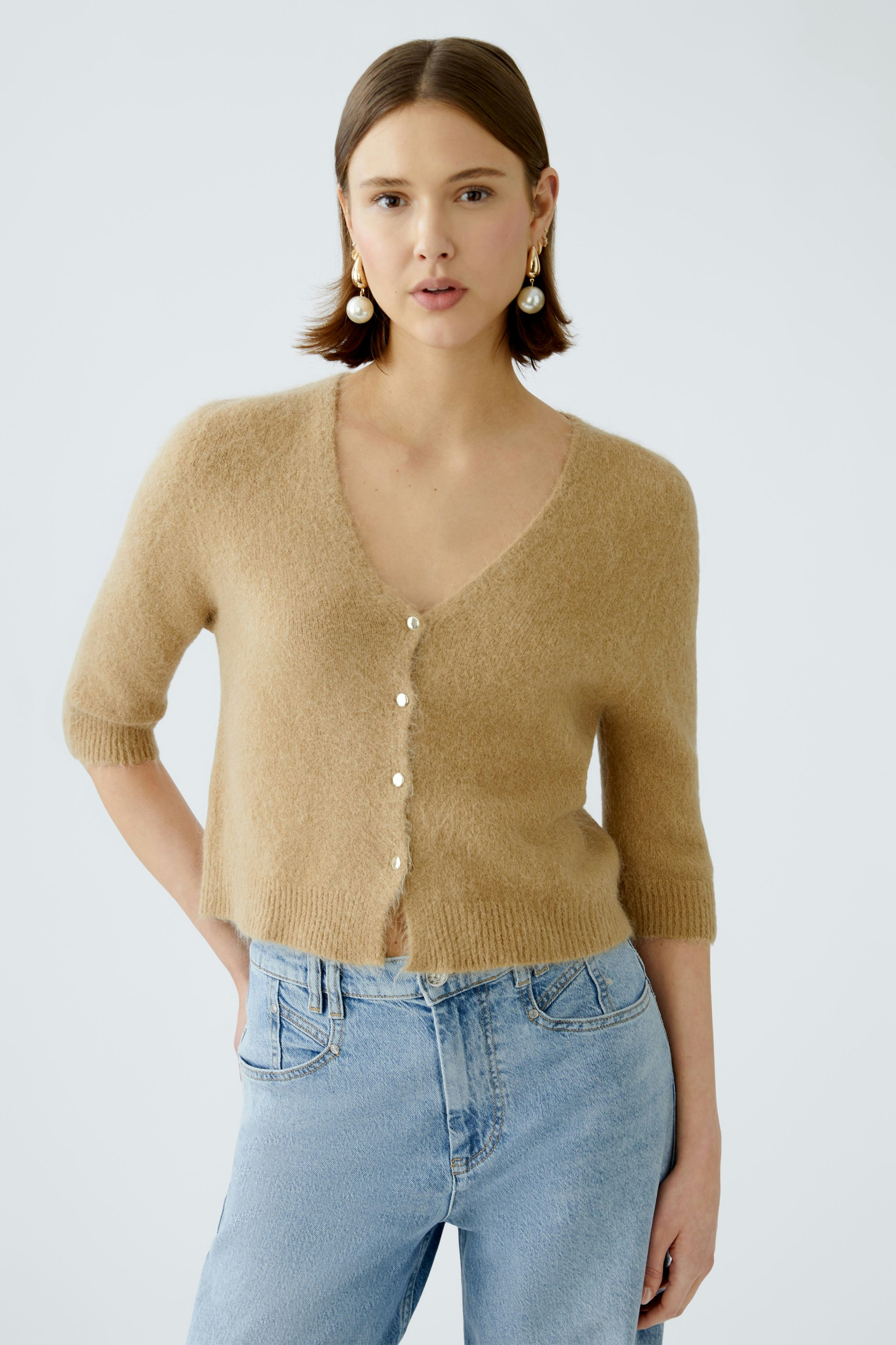 Stylish women's cardigan: A woman in a soft beige cardigan with buttons, paired with light blue jeans.