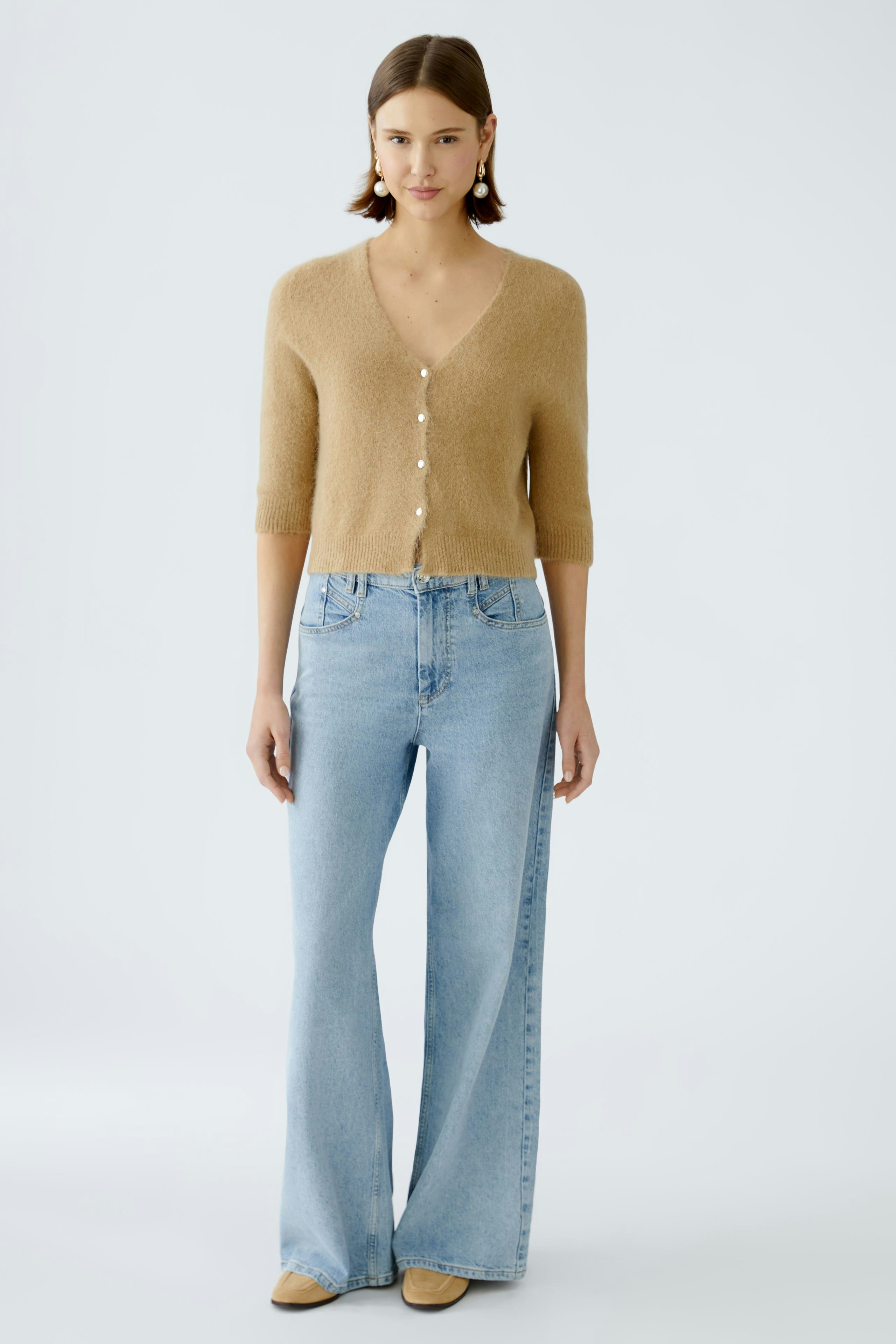 Stylish women's cardigan: A woman in a soft beige cardigan with buttons, paired with light blue jeans.