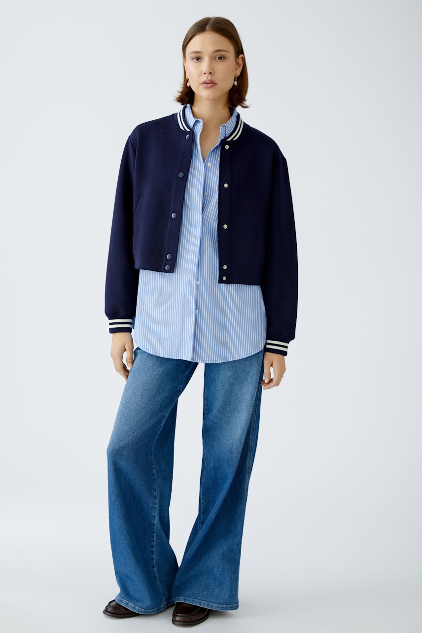 Stylish women's blouson: A woman in a navy bomber jacket over a striped shirt, exuding casual elegance.