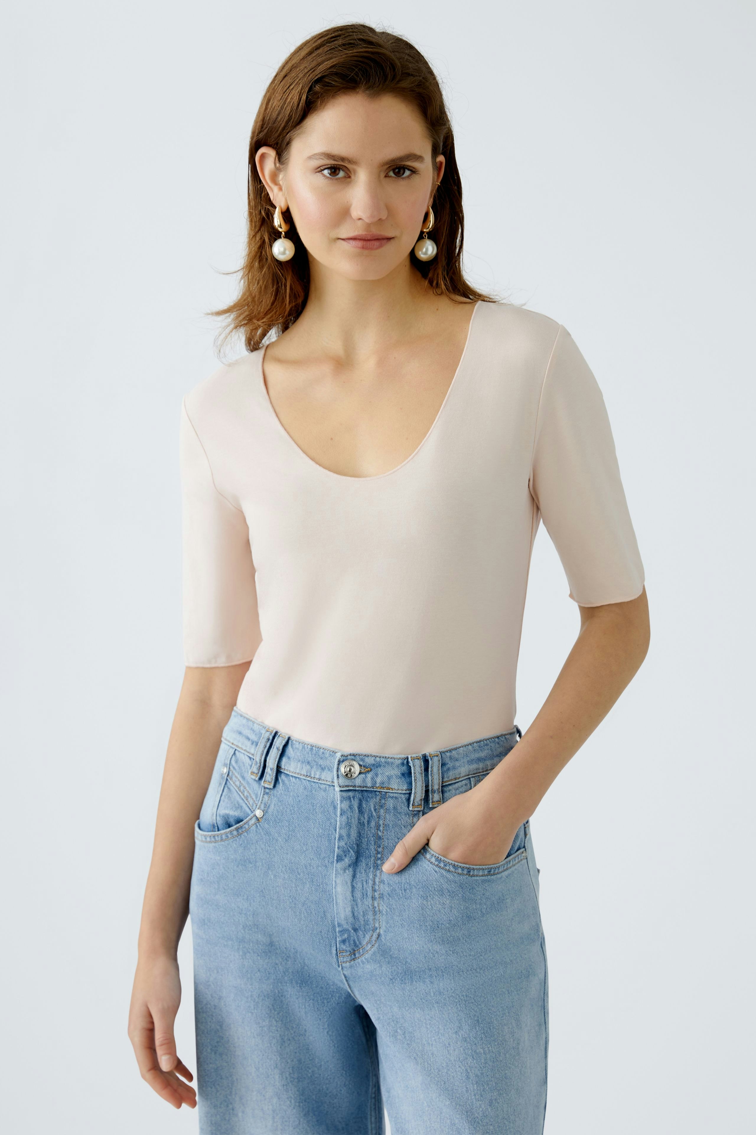 Elegant women's T-shirt: A woman in a soft pink top with short sleeves and a deep neckline.