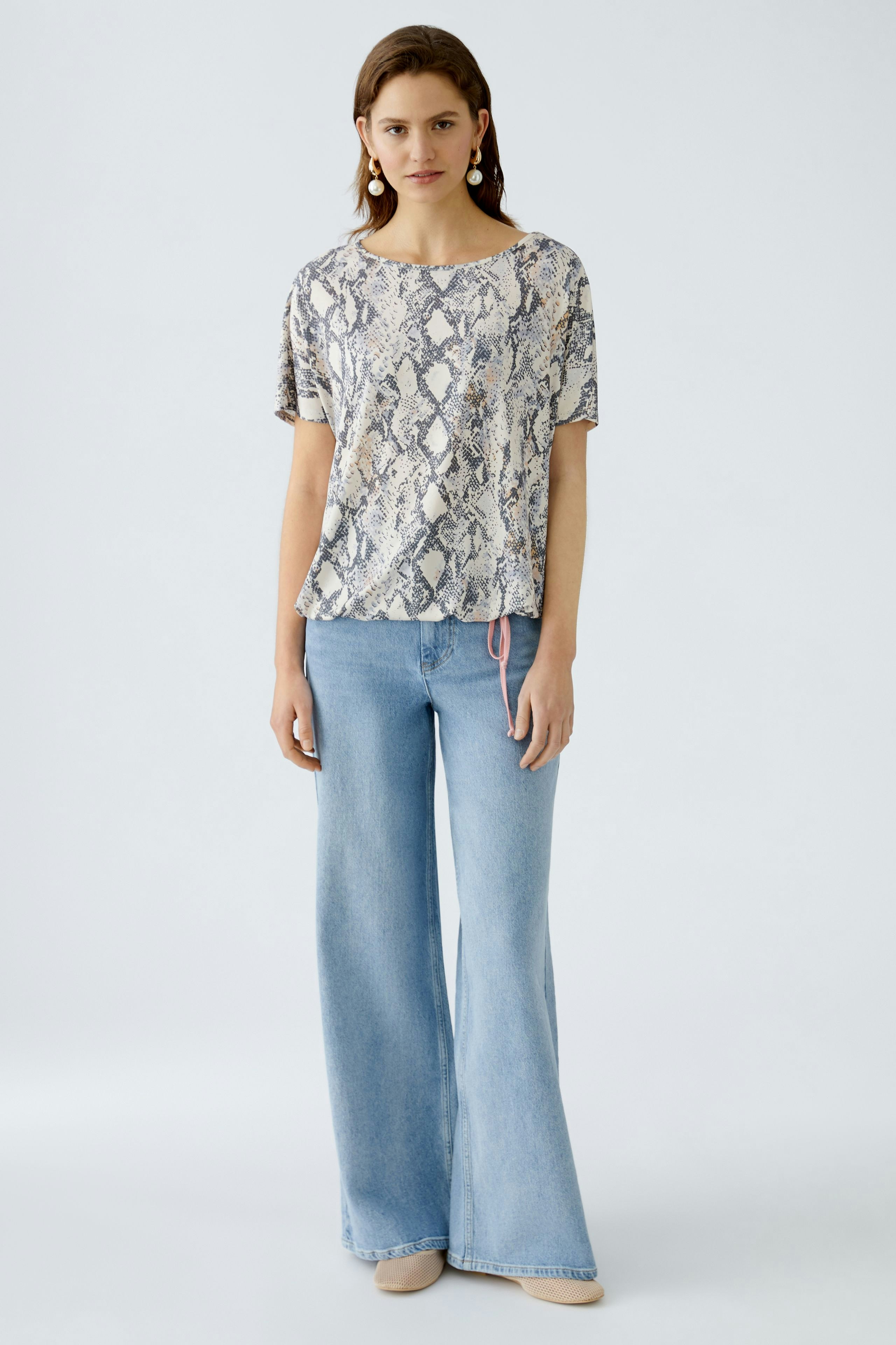 Damen-T-Shirt: Frau in schickem, gemustertem T-Shirt mit lässigen Jeans und eleganten Schuhen.