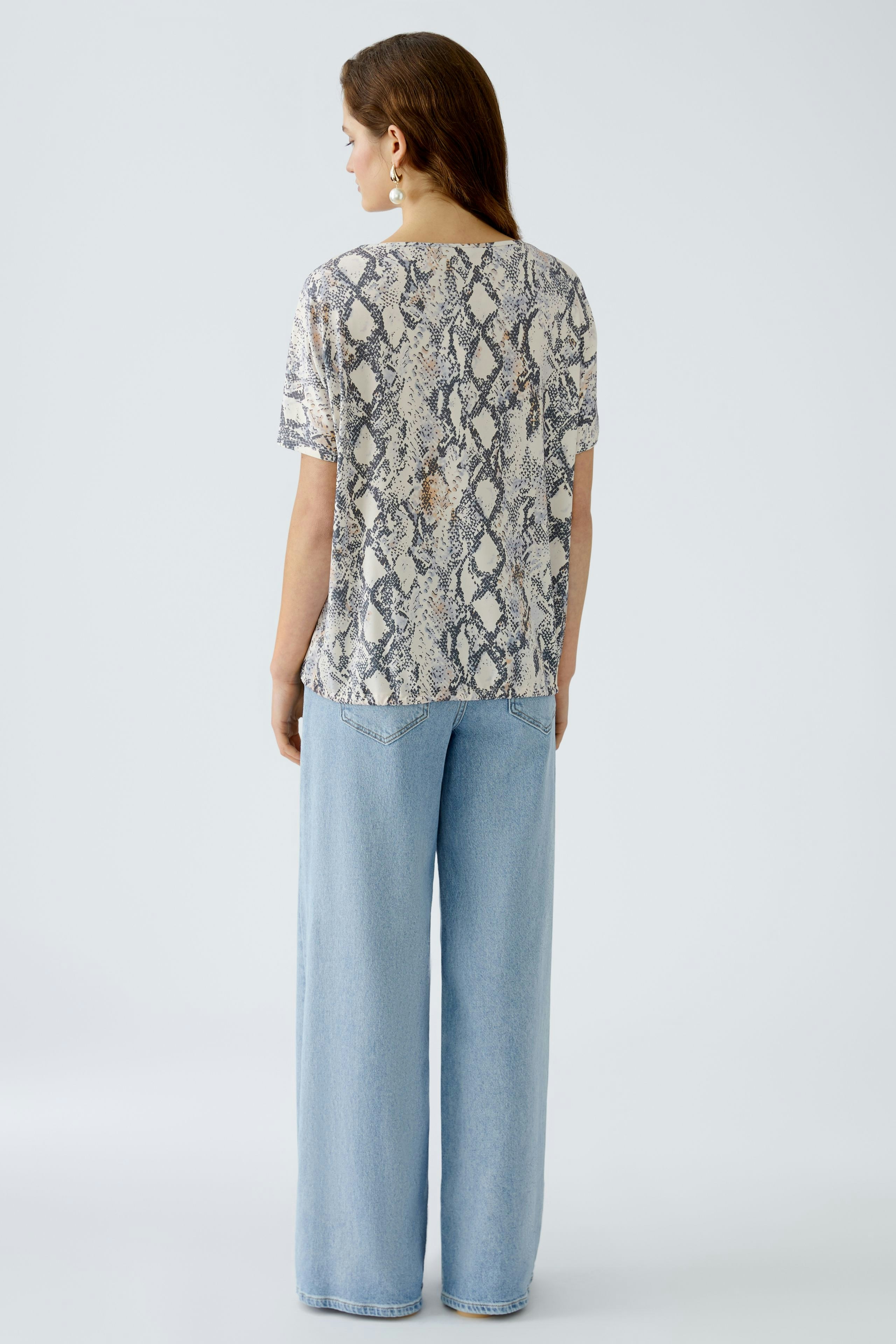 Damen-T-Shirt mit Schlangenmuster: Frau trägt ein leichtes, lässiges Oberteil in Kombination mit weiten Jeans.