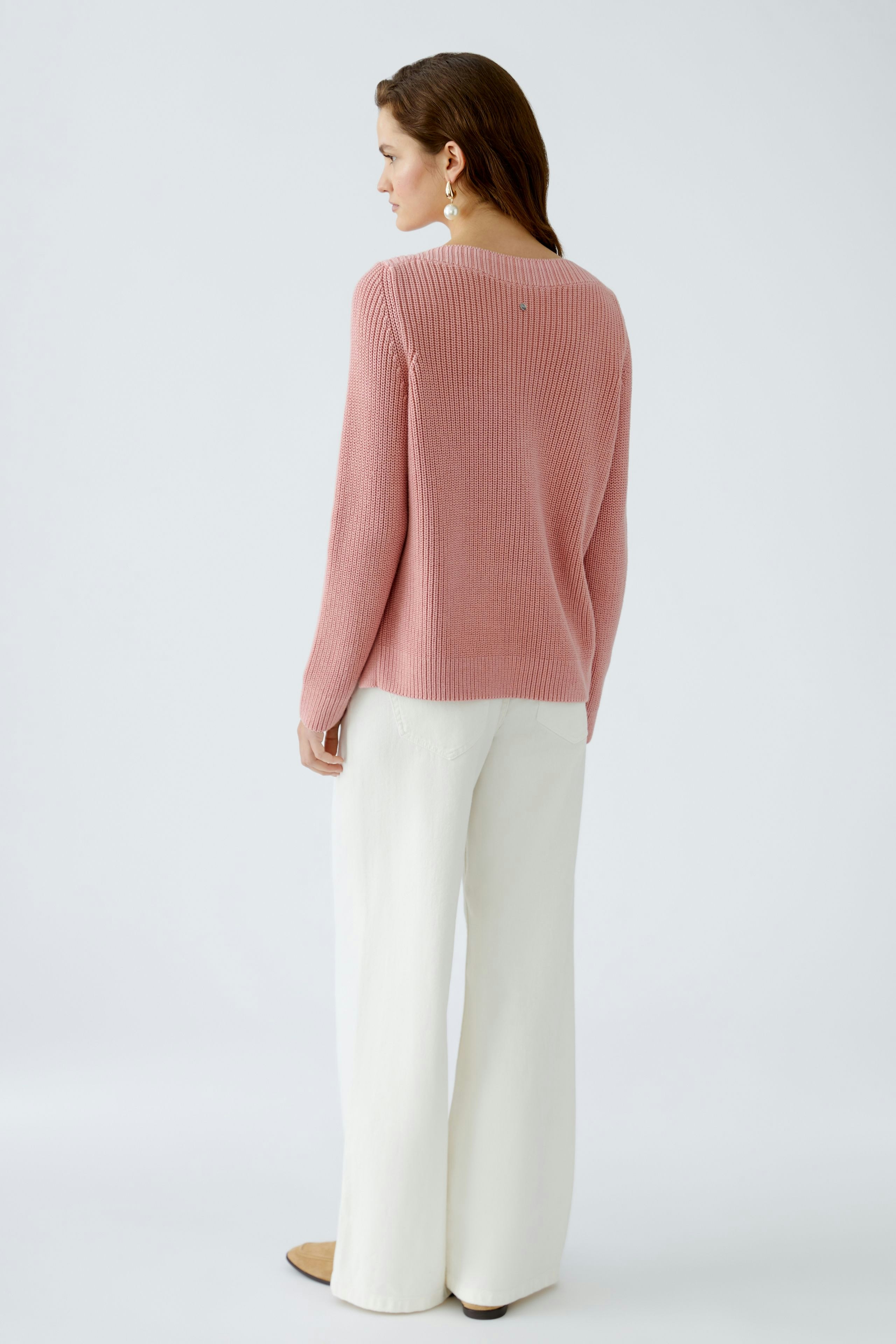 Stylish women's pullover: A woman in a soft pink pullover with a relaxed fit, paired with white trousers.