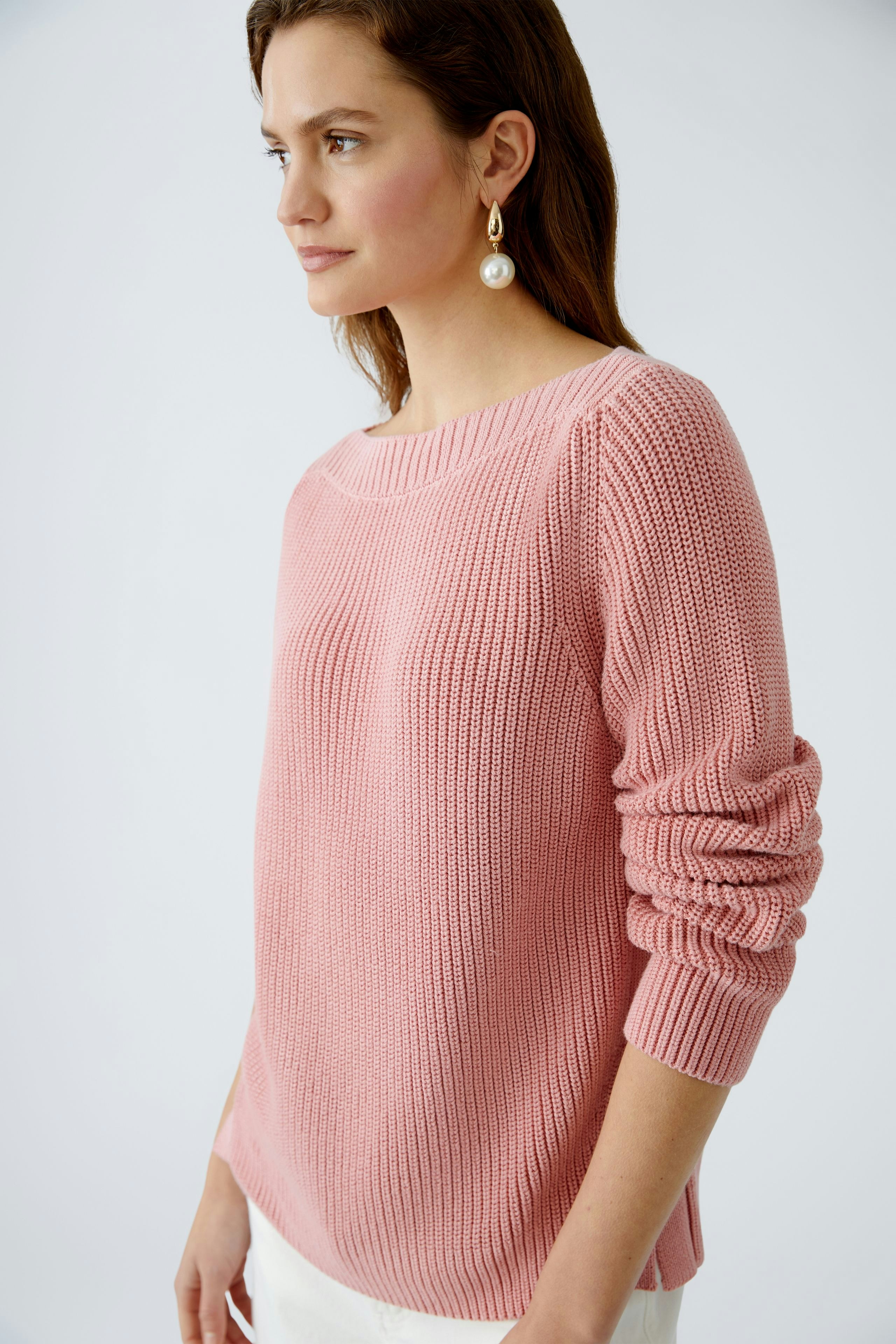 Modern women's pullover: A woman in a soft pink knit pullover with rolled sleeves.