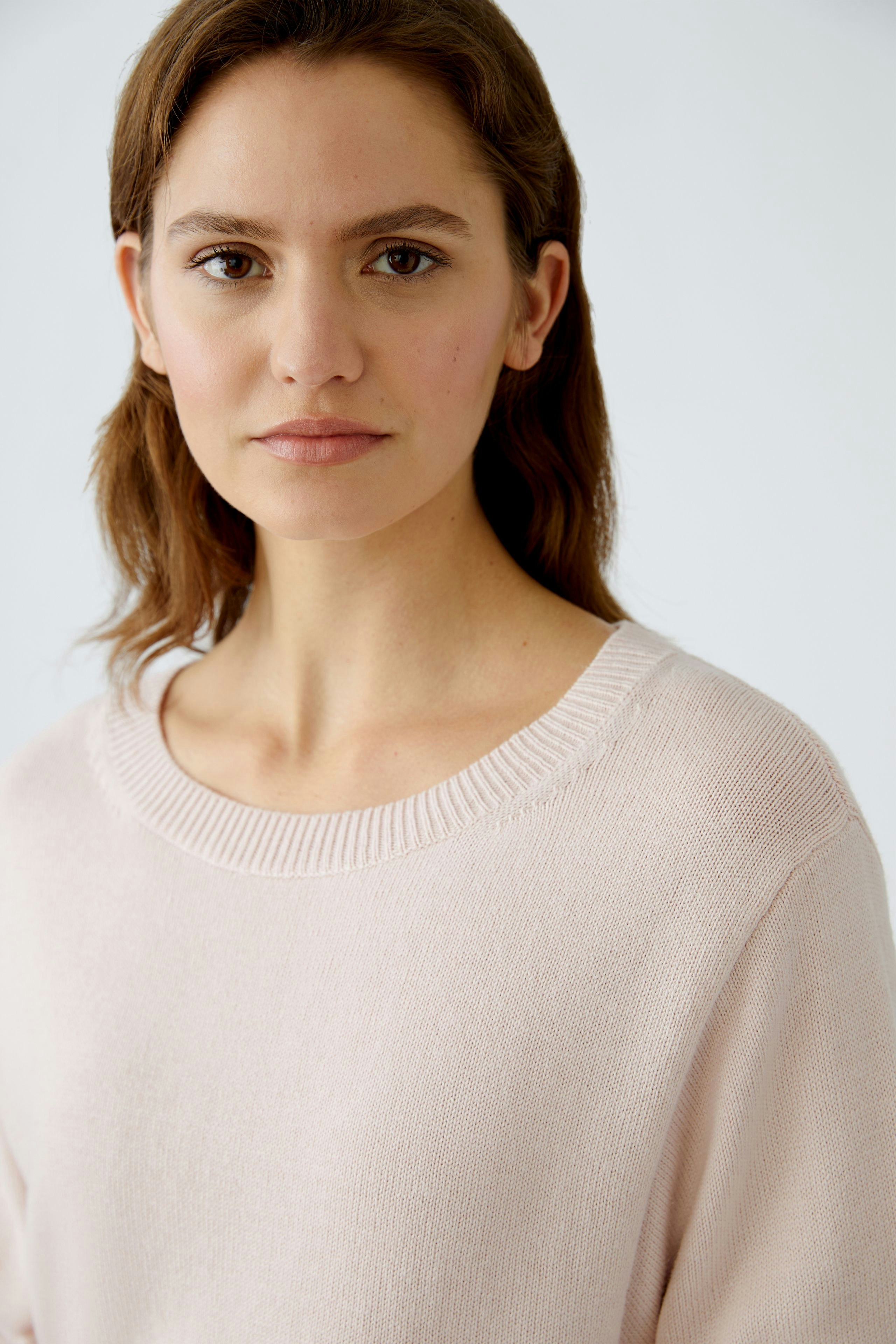 Modern women's pullover: A woman in a soft pink pullover with a relaxed fit and round neckline.