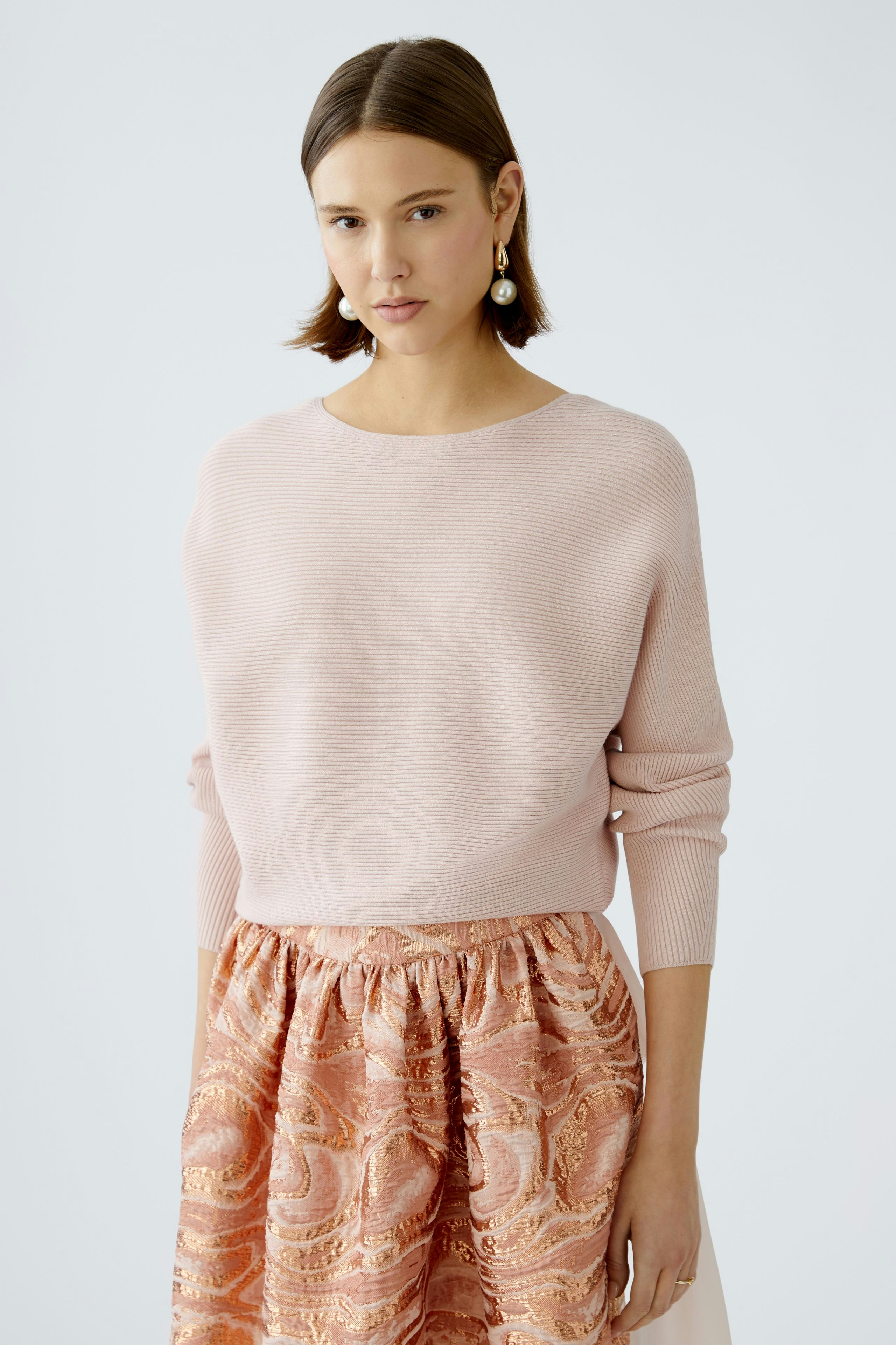 Damen-Pullover: Junge Frau in einem zarten rosa Pullover mit lässigem Schnitt und eleganter, gemusterter Hose.