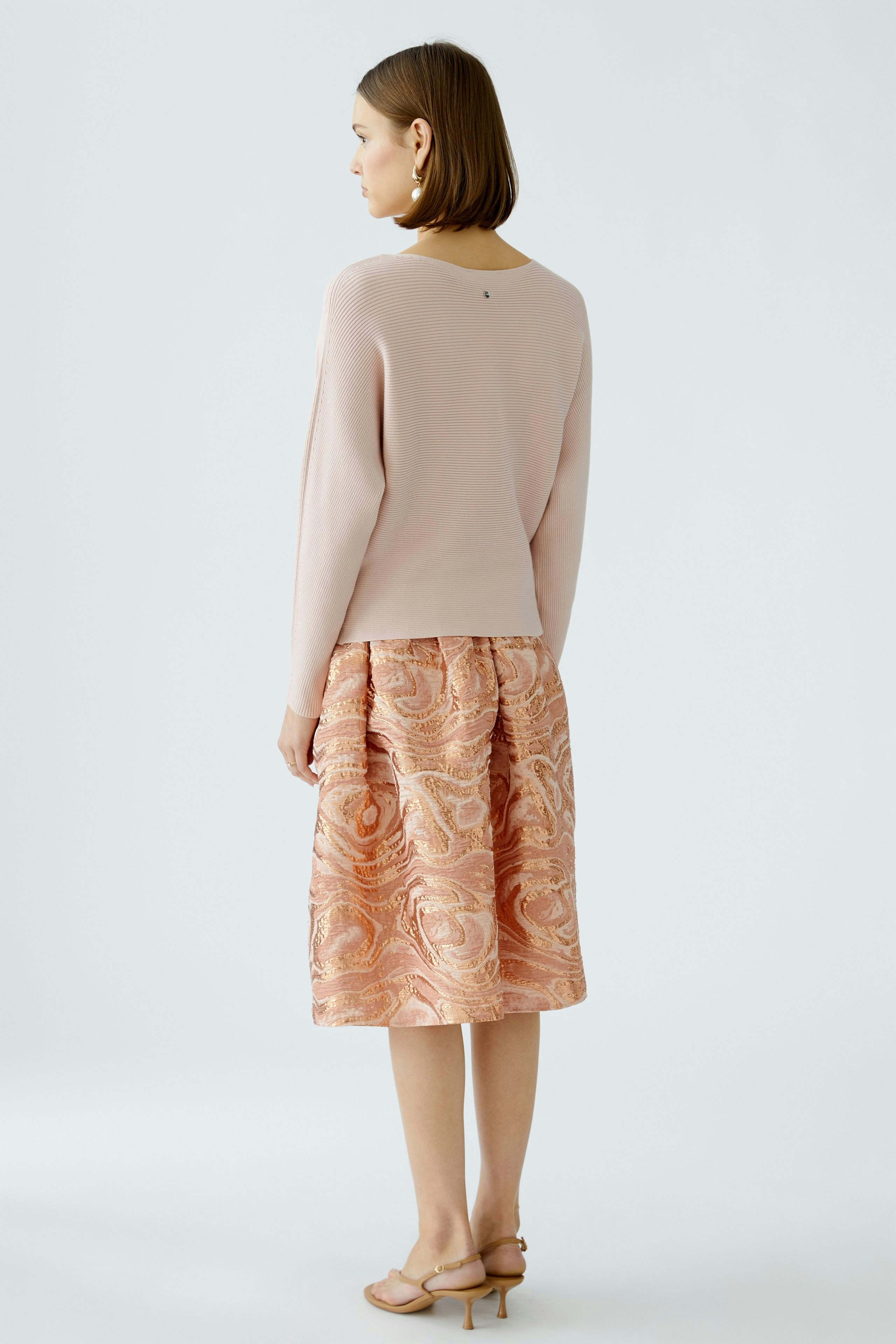 Damen-Pullover: Frau in zartem rosa Pullover, kombiniert mit einem eleganten Rock, von hinten zu sehen.