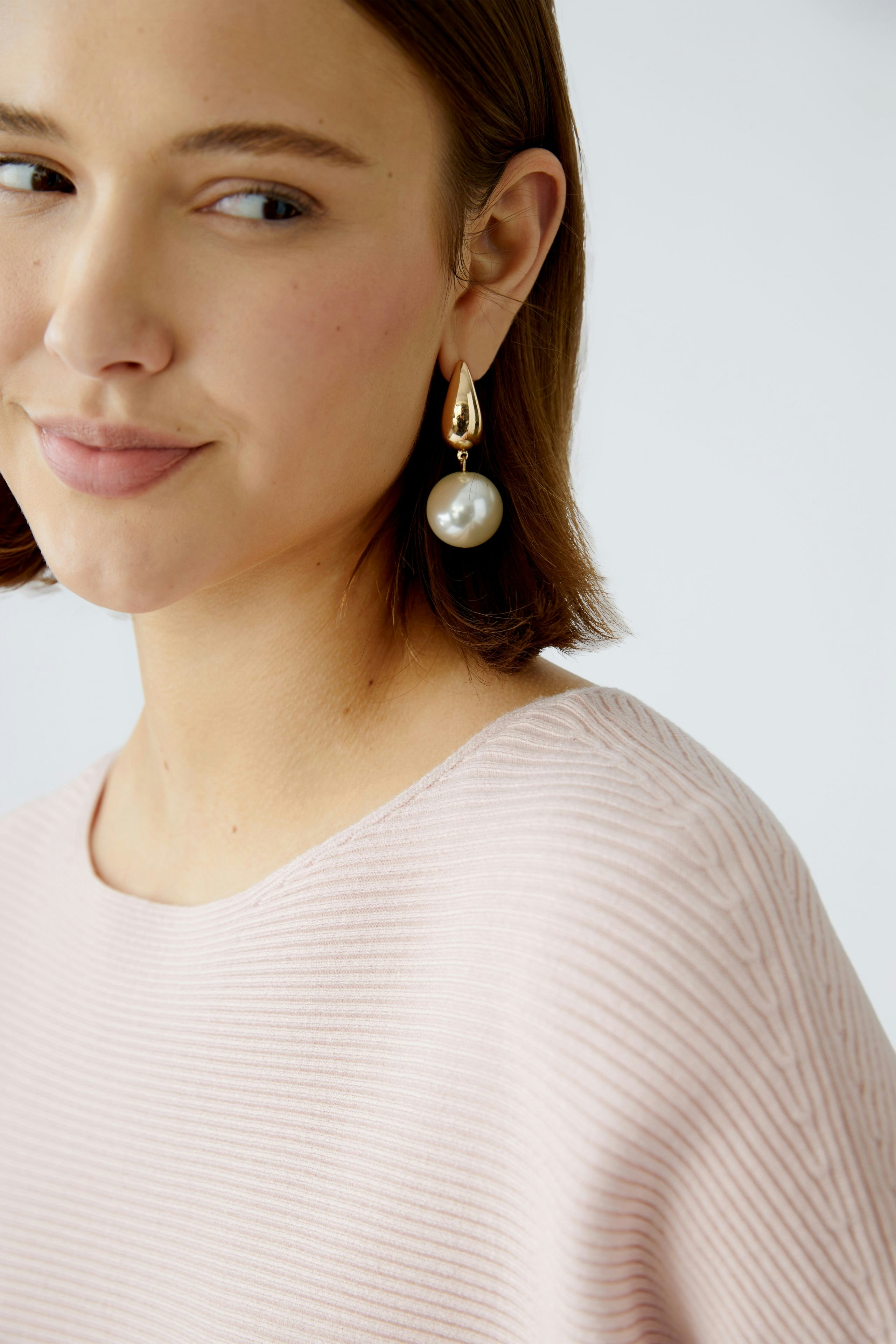 Eleganter Damen-Pullover: Frau mit zartem, rosa Pullover und auffälligen Ohrringen lächelt sanft.