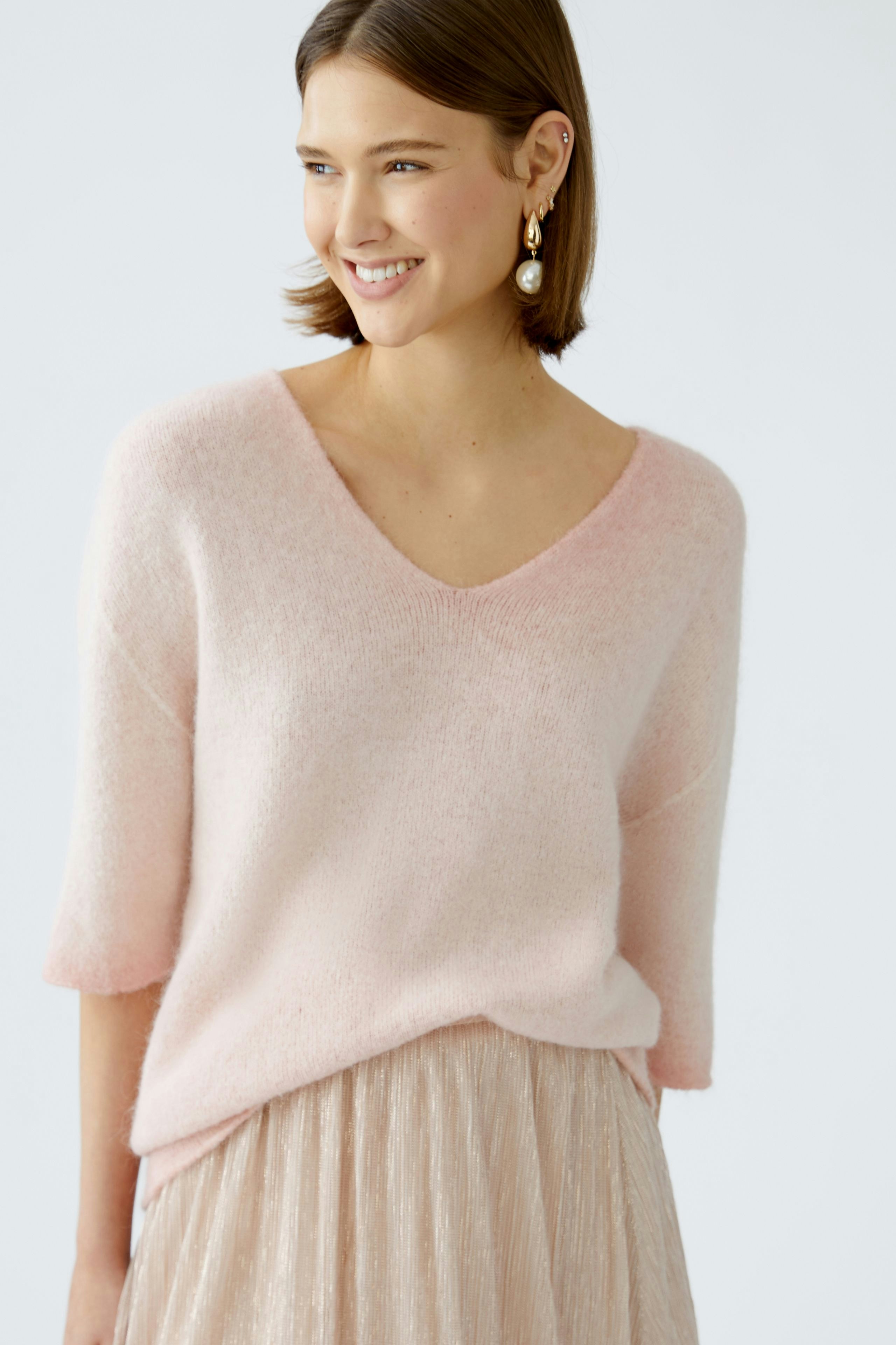 Modern women's pullover: A woman smiles in a soft pink pullover with a V-neck, paired with a flowing skirt.