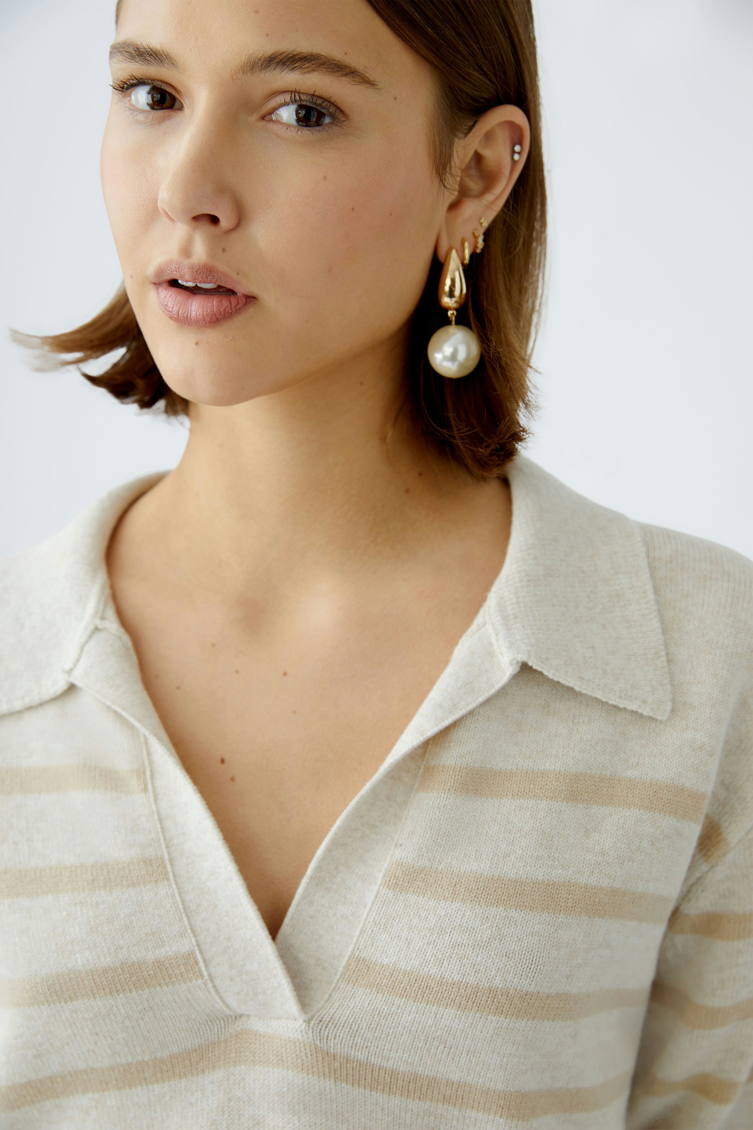 Stylish women's pullover: Close-up of a woman in a beige striped pullover with a collar.