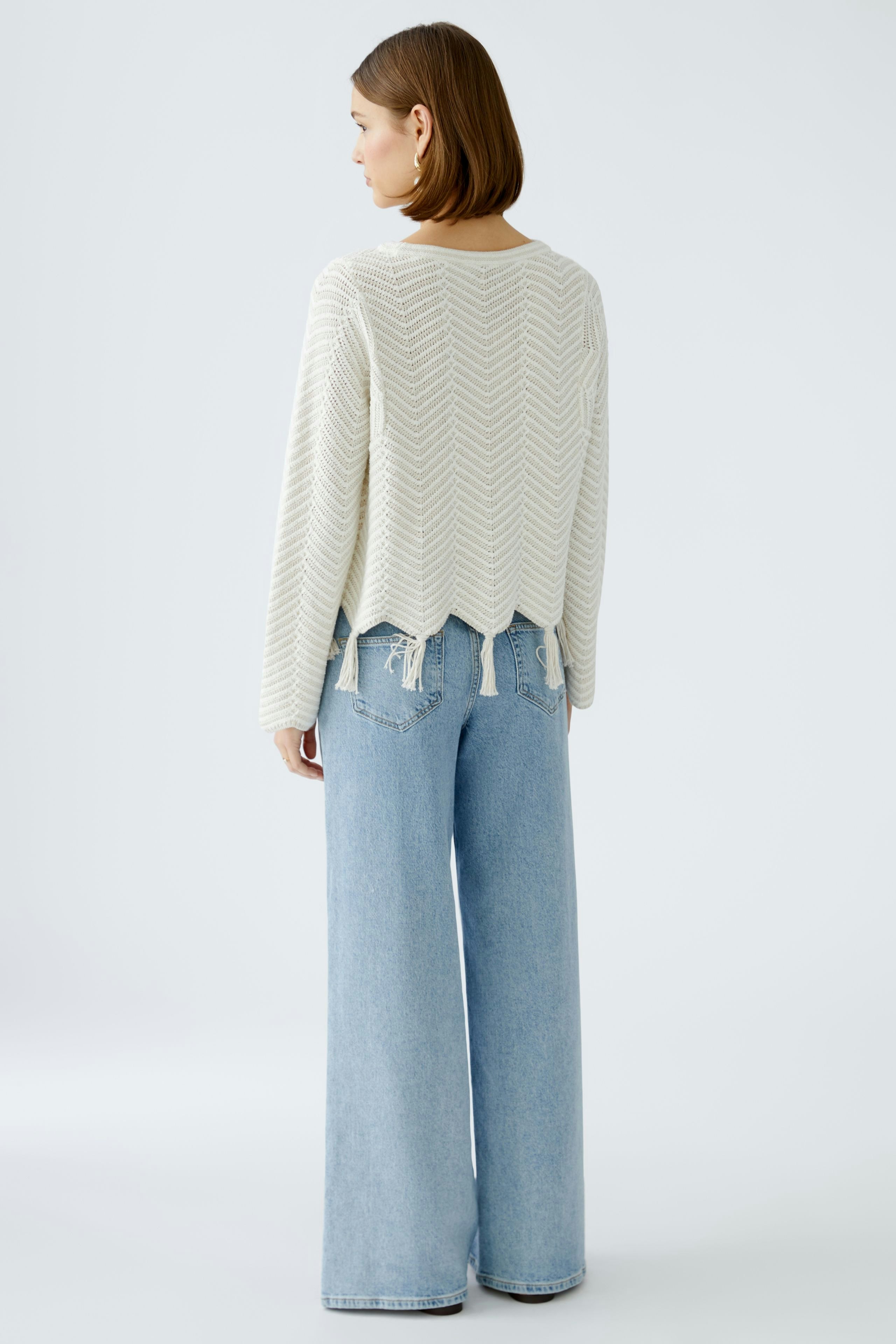 Damen-Pullover: Frau in einem hellen, strukturierten Pullover mit Wellenmuster und lässigen Jeans.